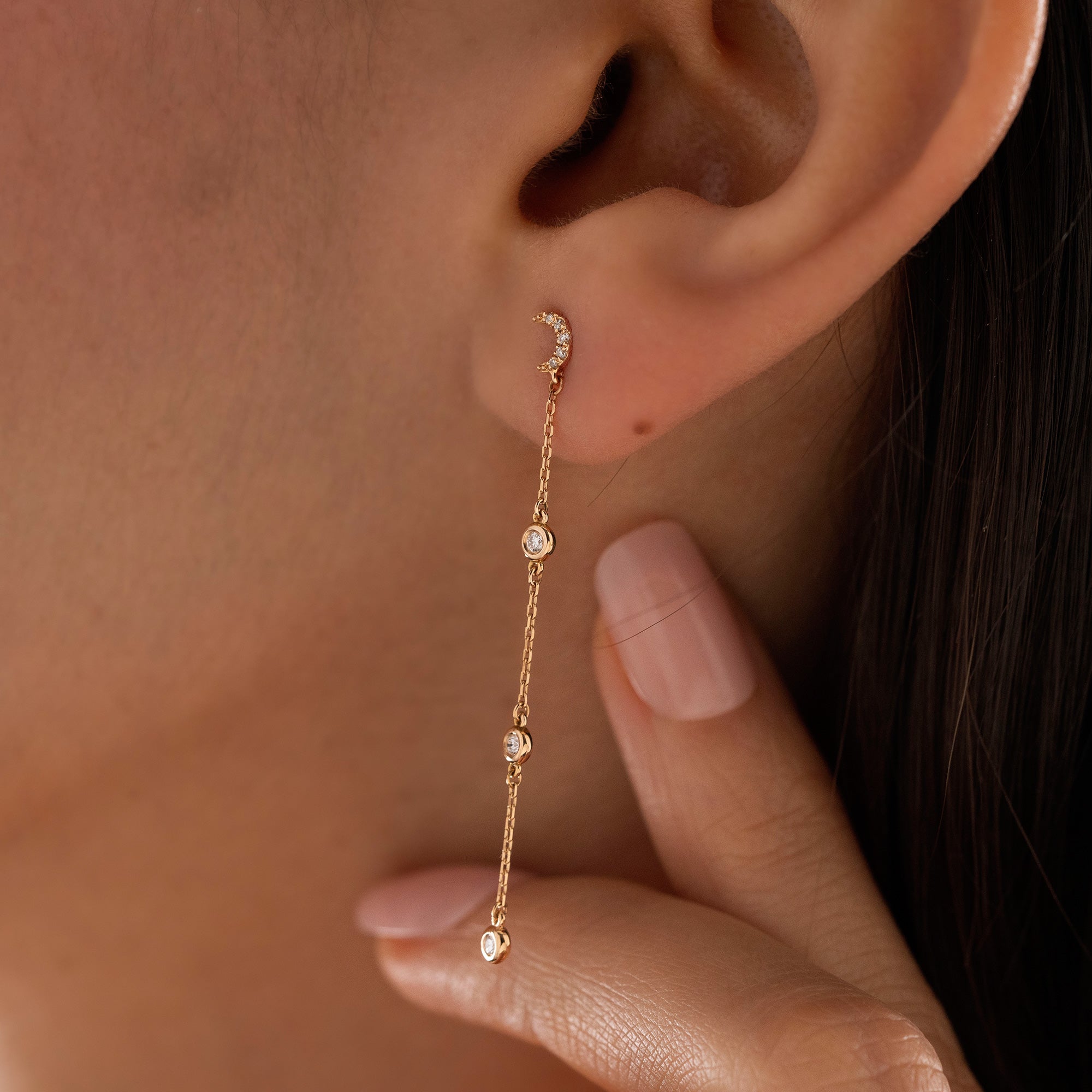 Arel Custom Jewelry 14k solid gold celestial crescent moon drop earring with dangling bezel set diamonds on a model.