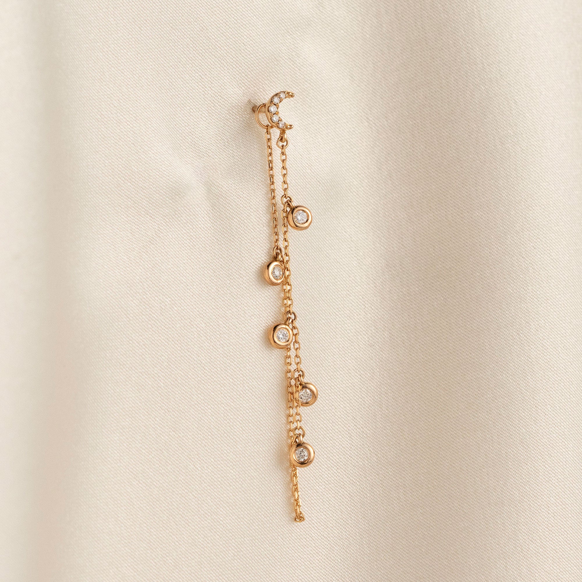 14k solid gold drape chain earring featuring a pave diamond crescent moon stud and bezel diamonds on a model