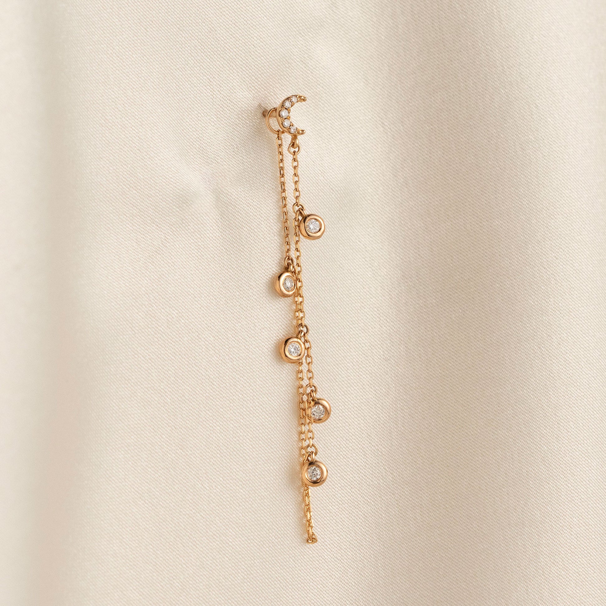 14k solid gold drape chain earring featuring a pave diamond crescent moon stud and bezel diamonds on a model