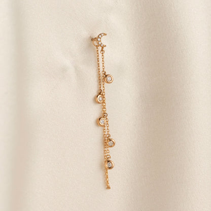 14k solid gold drape chain earring featuring a pave diamond crescent moon stud and bezel diamonds on a model