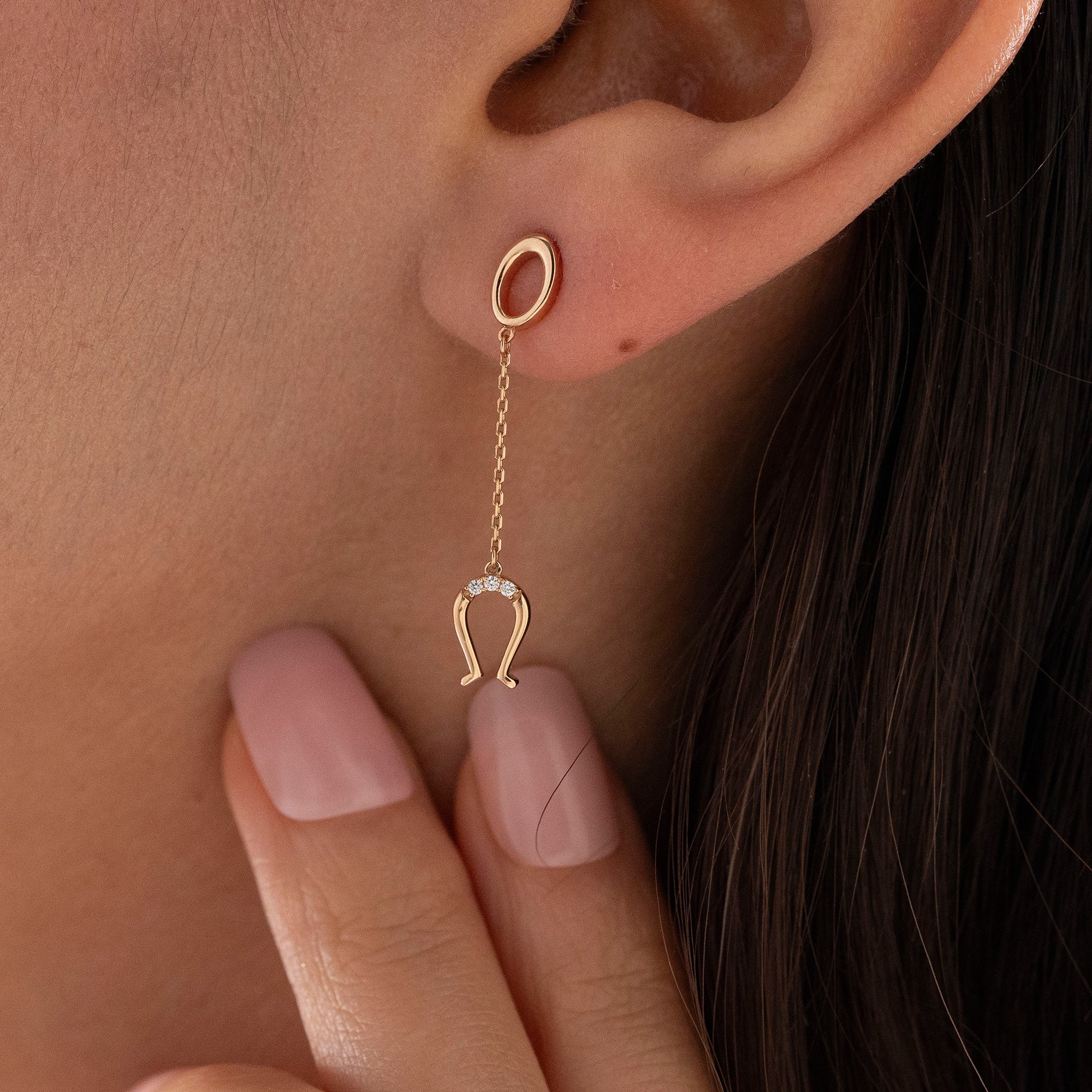 Arel Custom Jewelry 14k solid gold drop earring featuring an oval loop stud and dangling diamond horseshoe charm on a model.