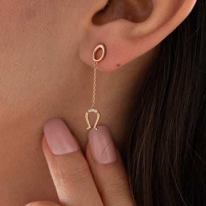 Arel Custom Jewelry 14k solid gold drop earring featuring an oval loop stud and dangling diamond horseshoe charm on a model.