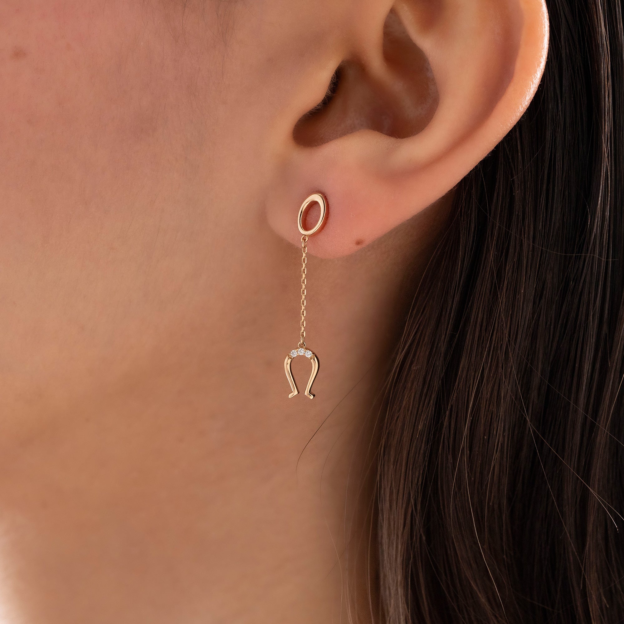 Arel Custom Jewelry 14k solid gold drop earring featuring an oval loop stud and dangling diamond horseshoe charm on a model.