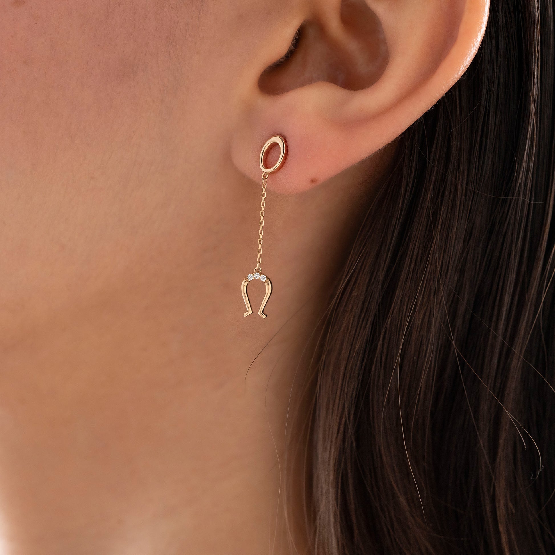 Arel Custom Jewelry 14k solid gold drop earring featuring an oval loop stud and dangling diamond horseshoe charm on a model.
