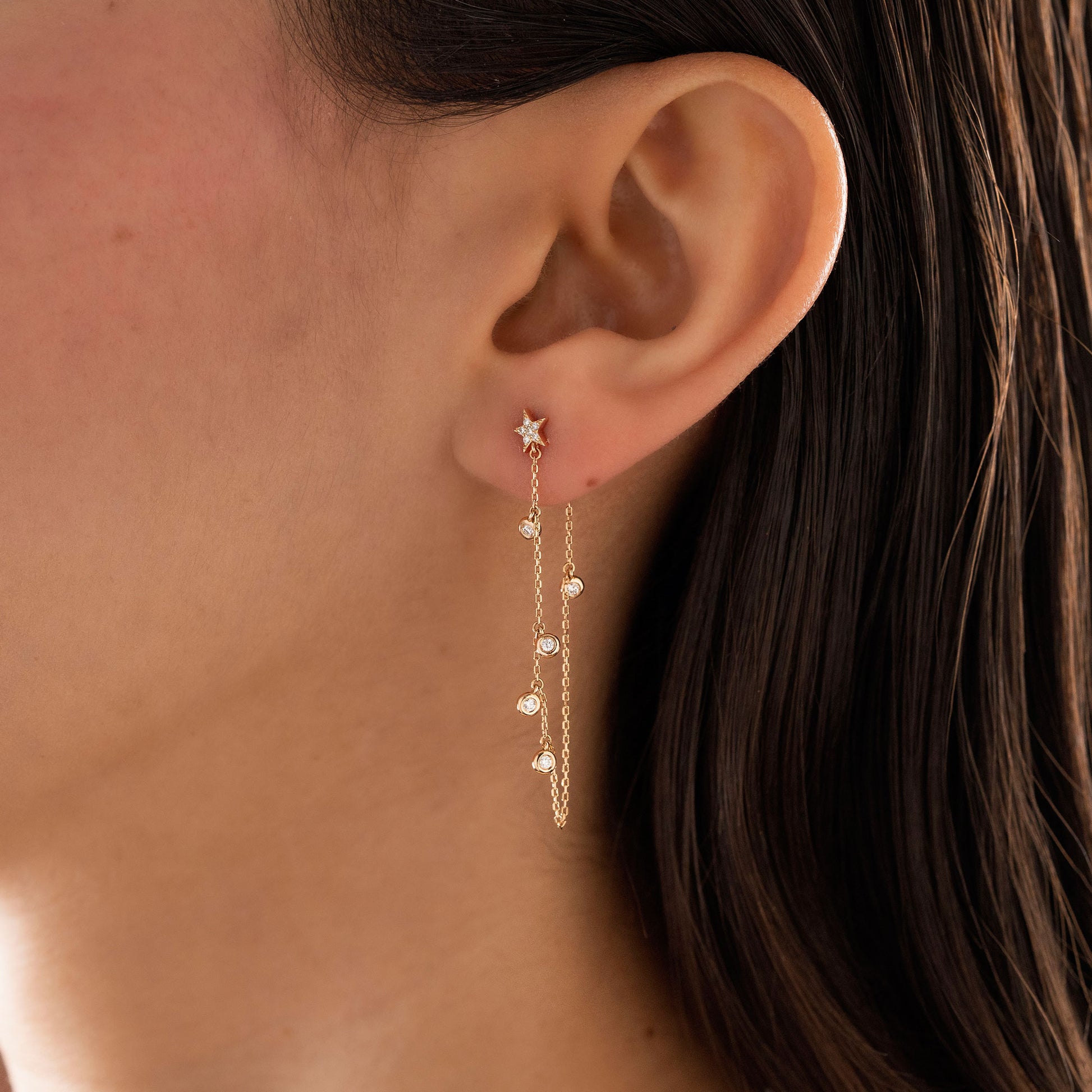 Dainty 14k gold front-to-back chain earring featuring a diamond star stud and bezel-set diamond drops on a model.