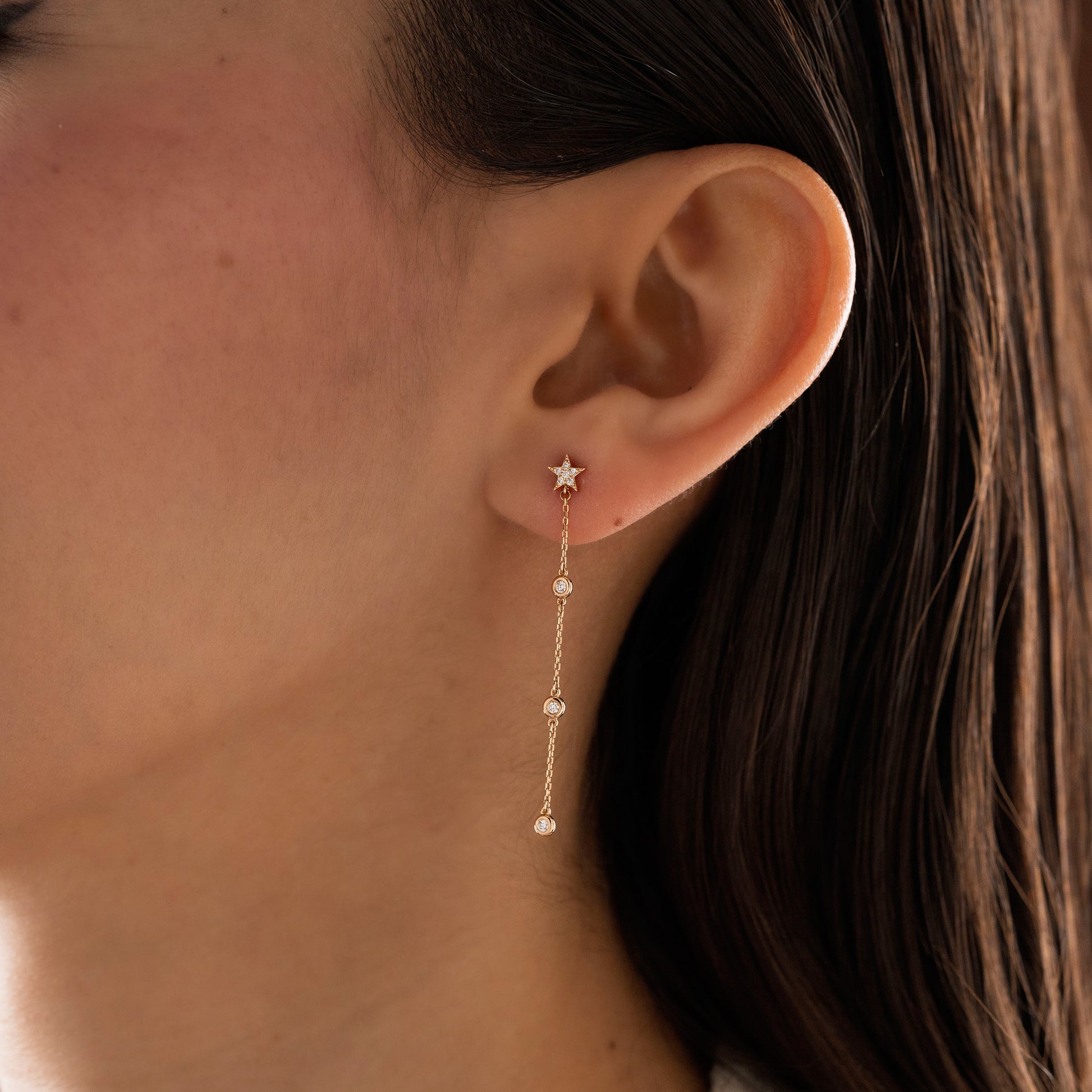 Arel Custom Jewelry 14k solid gold diamond star drop earring with dangling bezel set diamonds on a model.