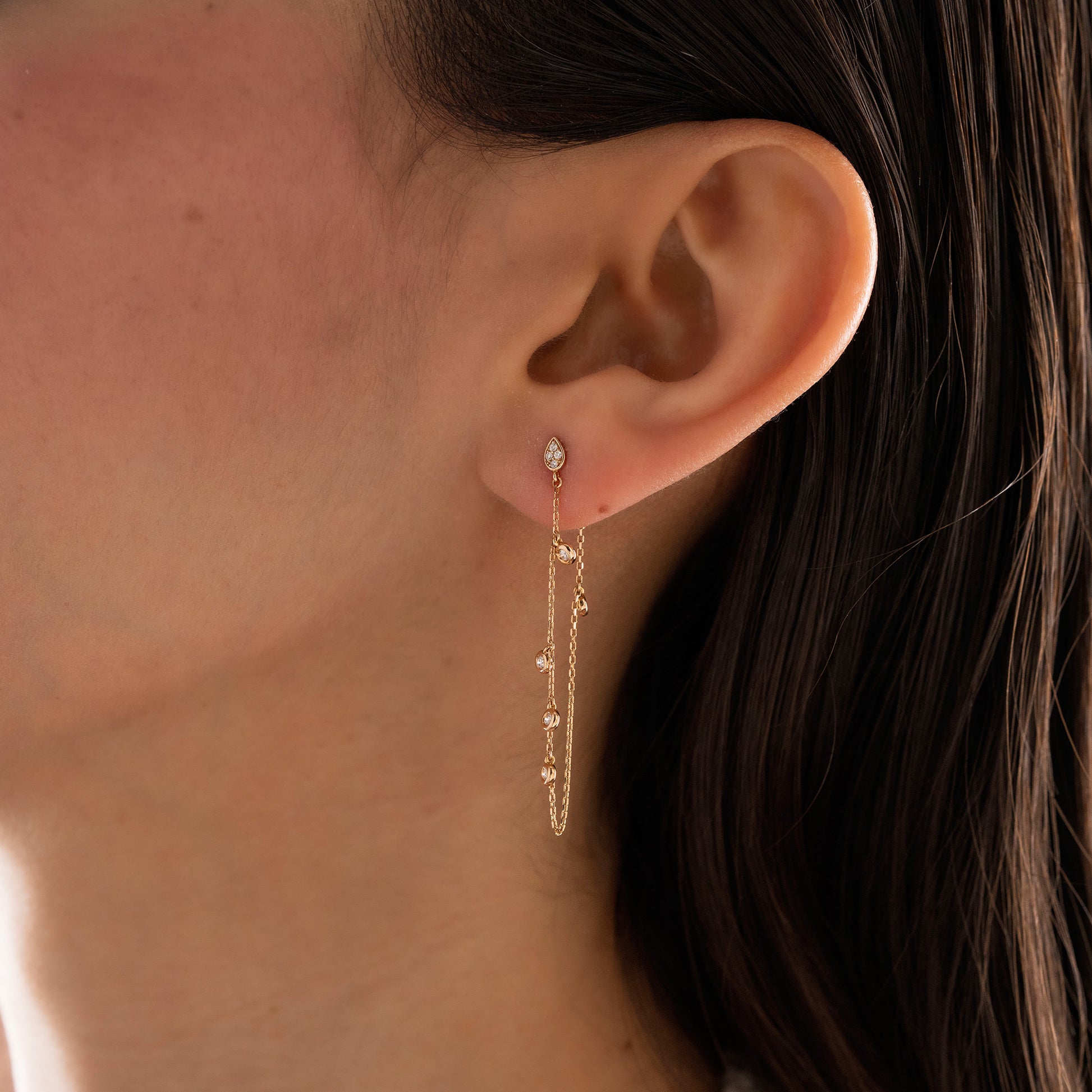 Arel Custom Jewelry 14k solid gold drape chain earring featuring a diamond teardrop stud and bezel diamonds on a model.