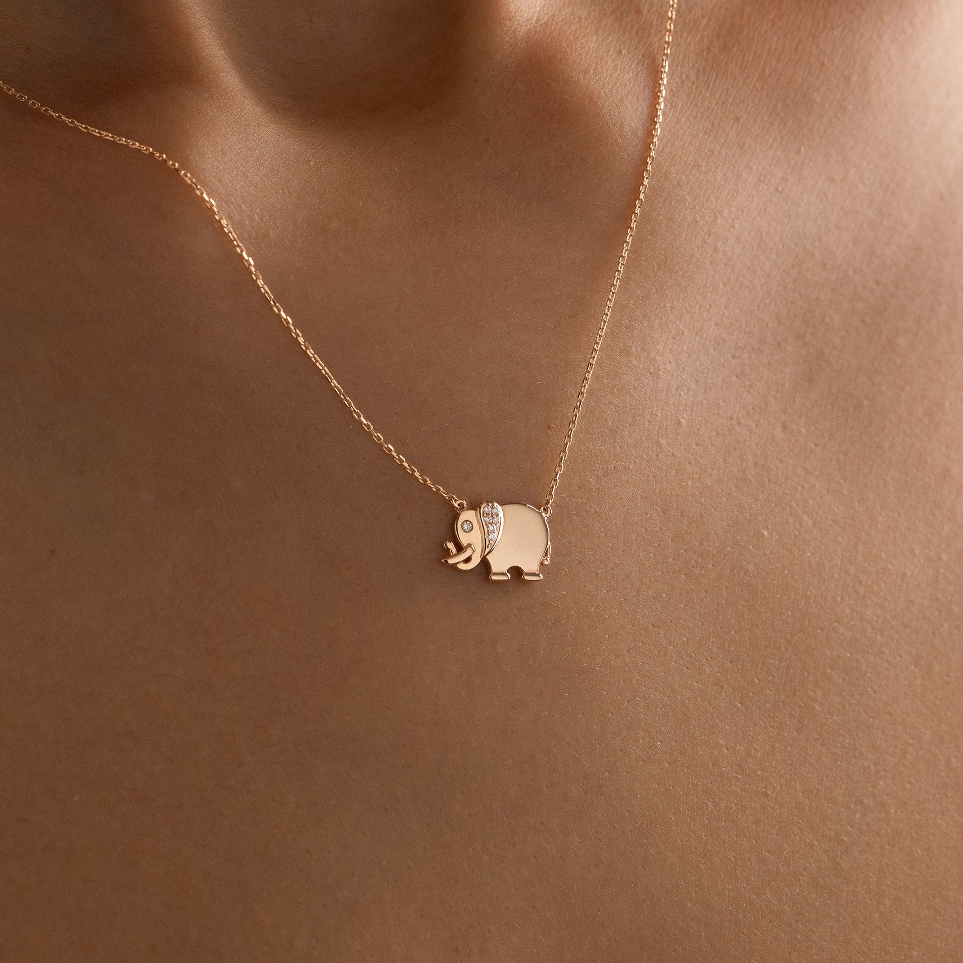 Arel Custom Jewelry 14k solid gold necklace featuring a polished elephant pendant with a pave diamond ear and trunk up on a model.