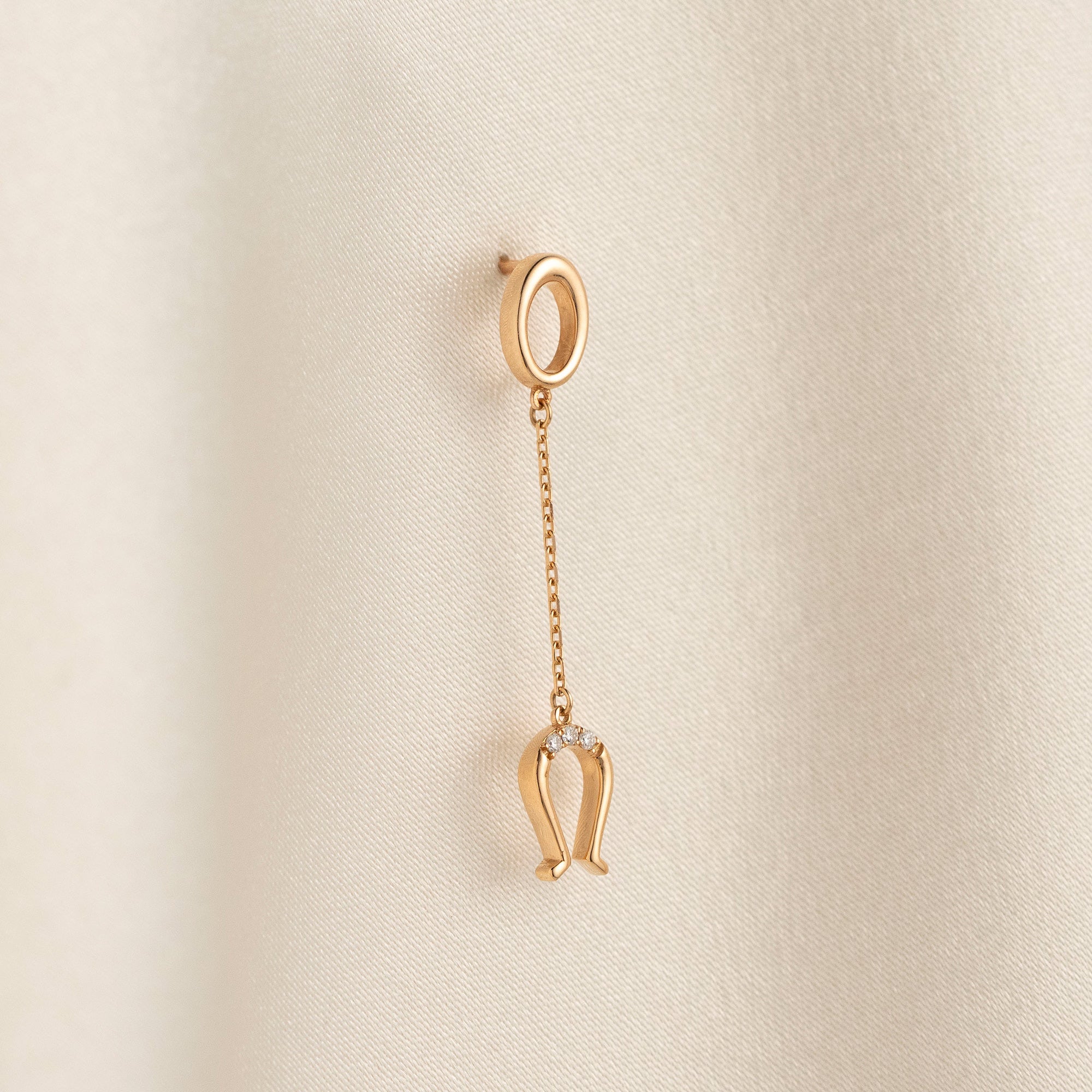 Arel Custom Jewelry 14k solid gold drop earring featuring an oval loop stud and dangling diamond horseshoe charm on a model.