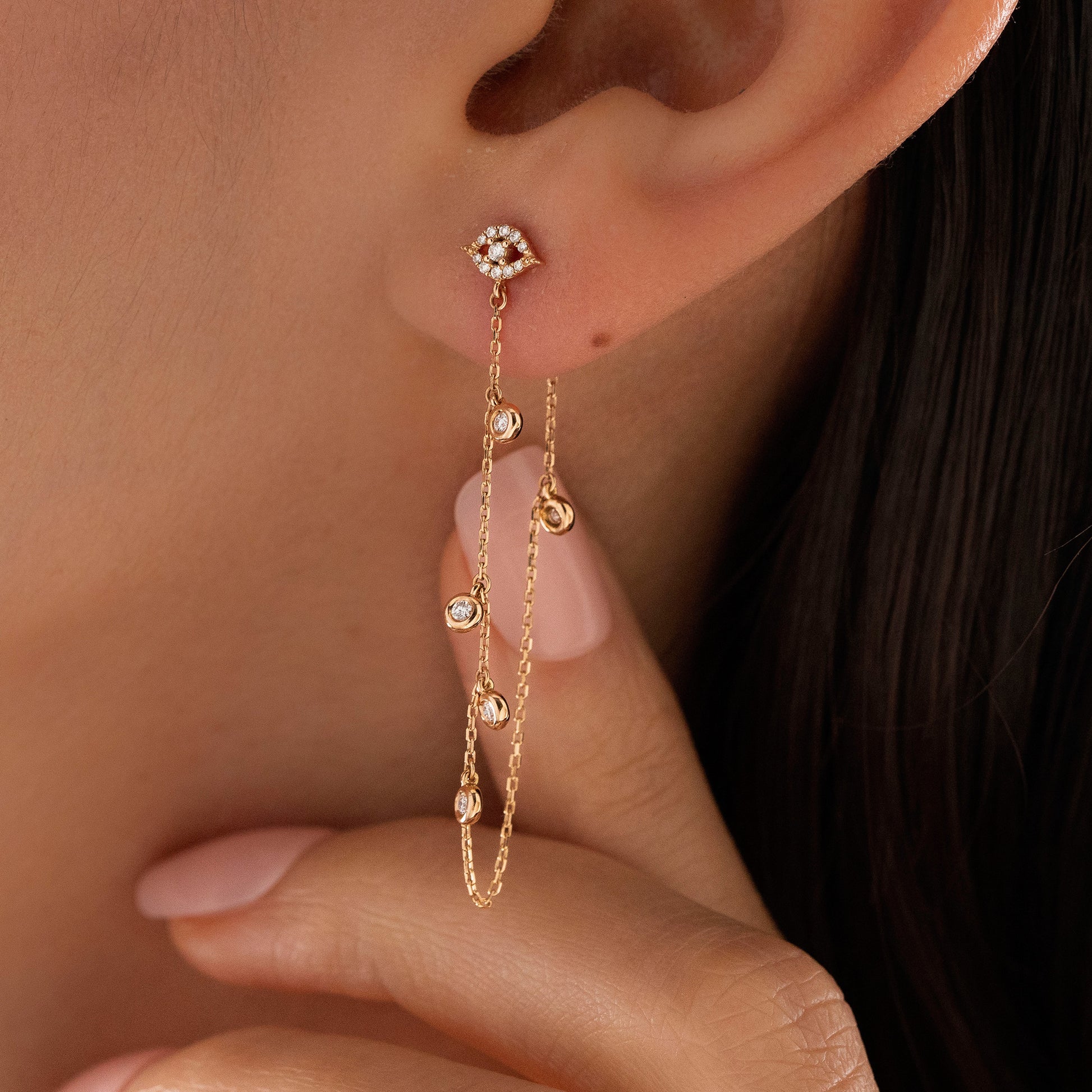 Arel Custom Jewelry 14k solid gold drape chain earring featuring a pave diamond evil eye stud and bezel diamonds on a model.