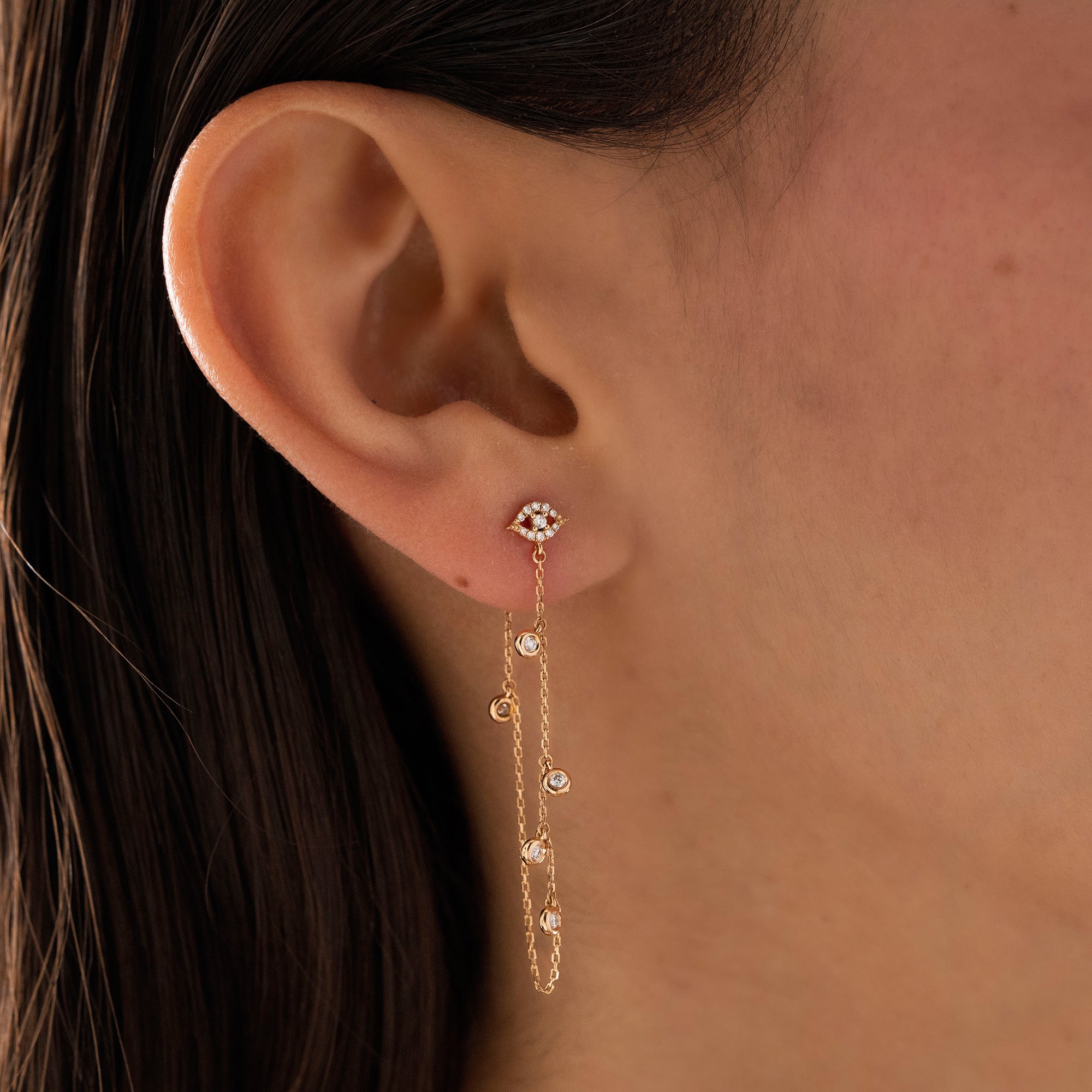 Arel Custom Jewelry 14k solid gold drape chain earring featuring a pave diamond evil eye stud and bezel diamonds on a model.