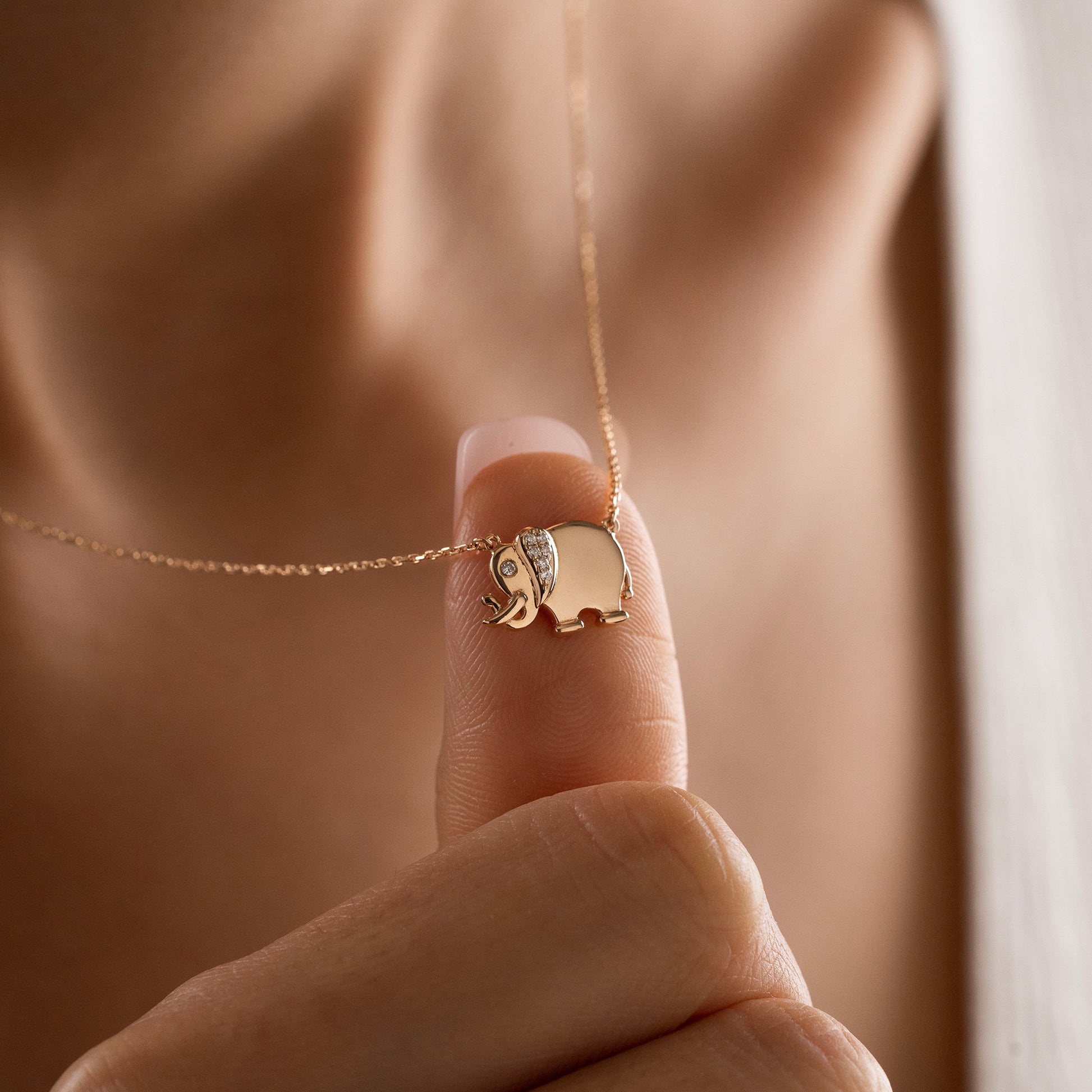 Arel Custom Jewelry 14k solid gold necklace featuring a polished elephant pendant with a pave diamond ear and trunk up on a model.