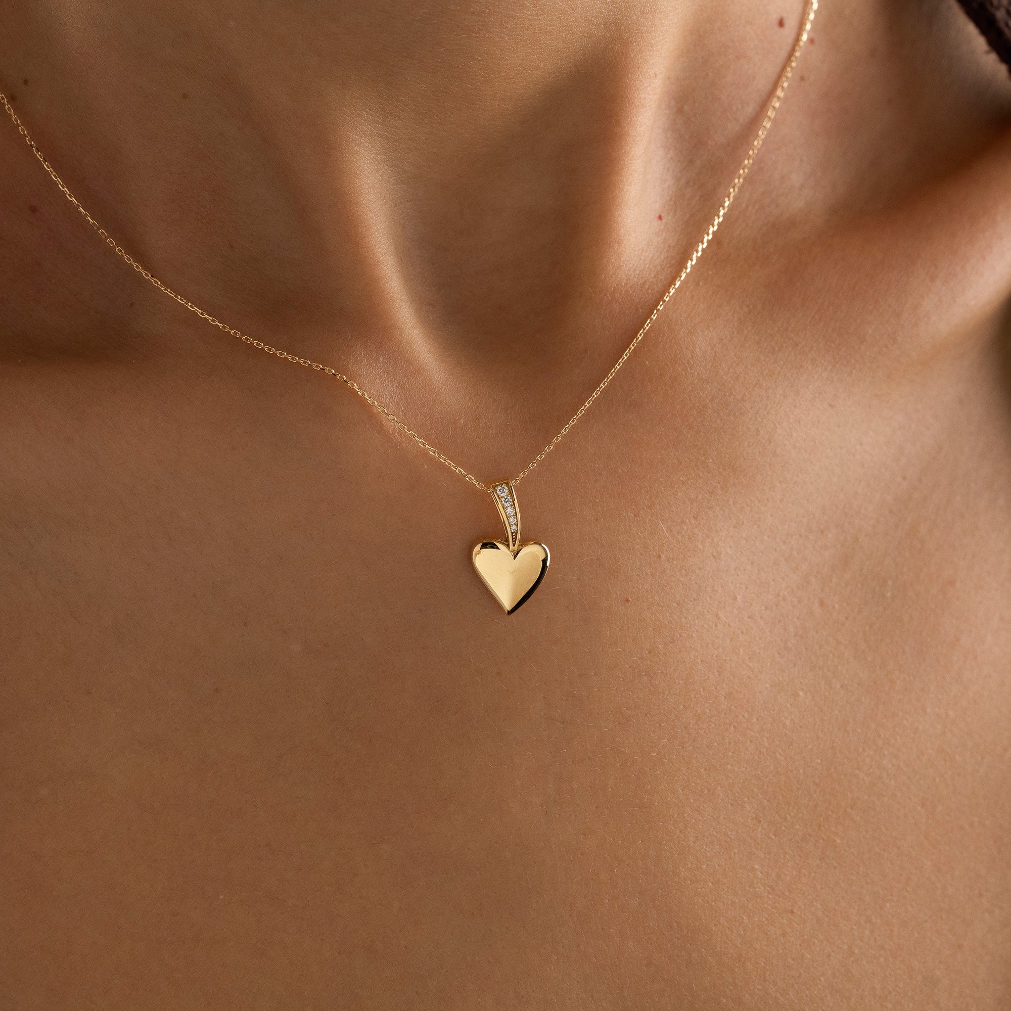 Arel Custom Jewelry 14k solid gold polished heart pendant featuring a pave diamond bail on a model.