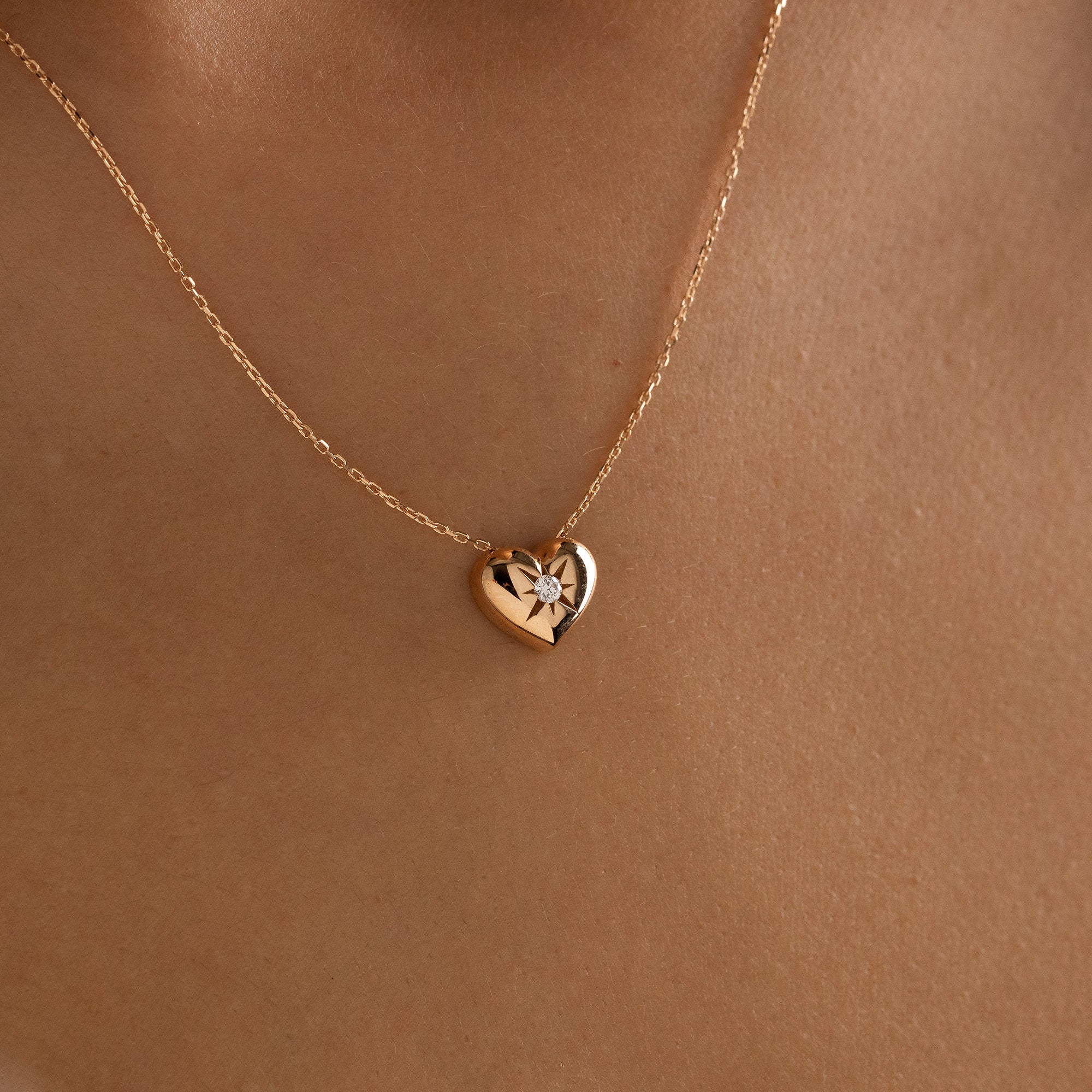 Arel Custom Jewelry 14k solid gold necklace featuring a polished puffed heart pendant with a starburst set center diamond on a model.