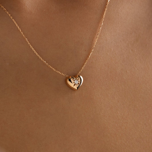 Arel Custom Jewelry 14k solid gold necklace featuring a polished puffed heart pendant with a starburst set center diamond on a model.