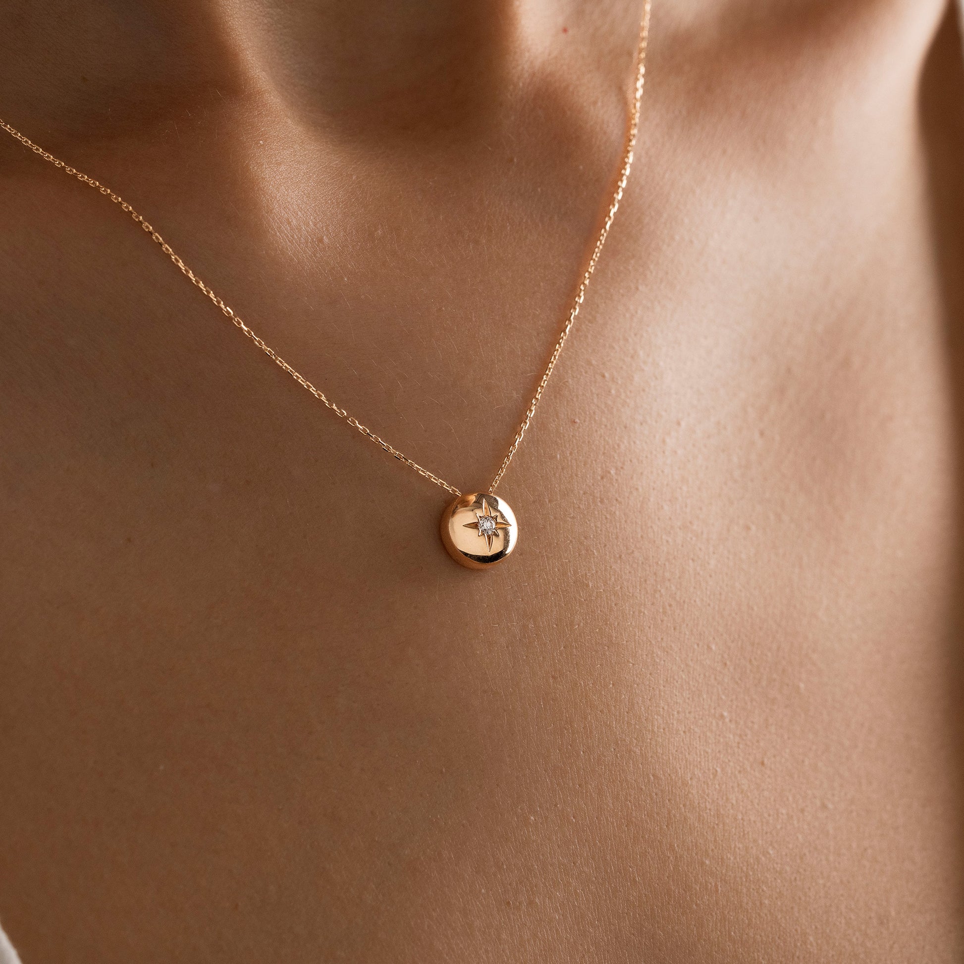 Arel Custom Jewelry 14k solid gold necklace featuring a polished domed pendant with a starburst set center diamond on a model.