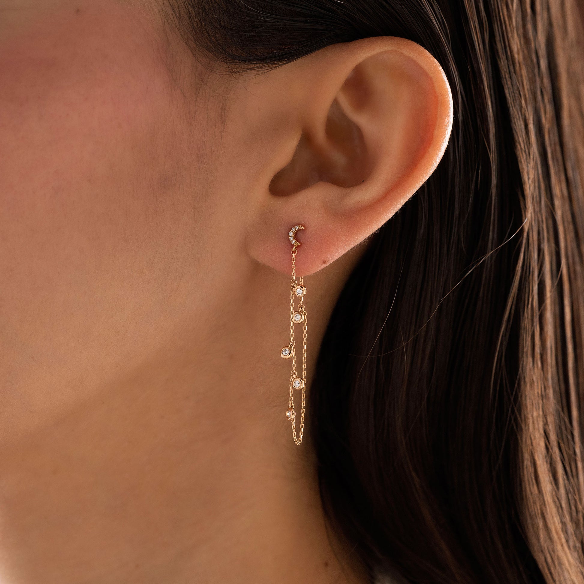14k solid gold drape chain earring featuring a pave diamond crescent moon stud and bezel diamonds on a model