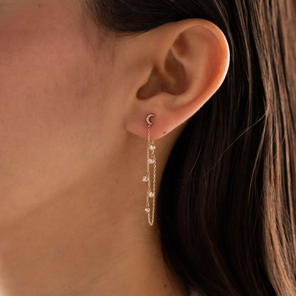 14k solid gold drape chain earring featuring a pave diamond crescent moon stud and bezel diamonds on a model