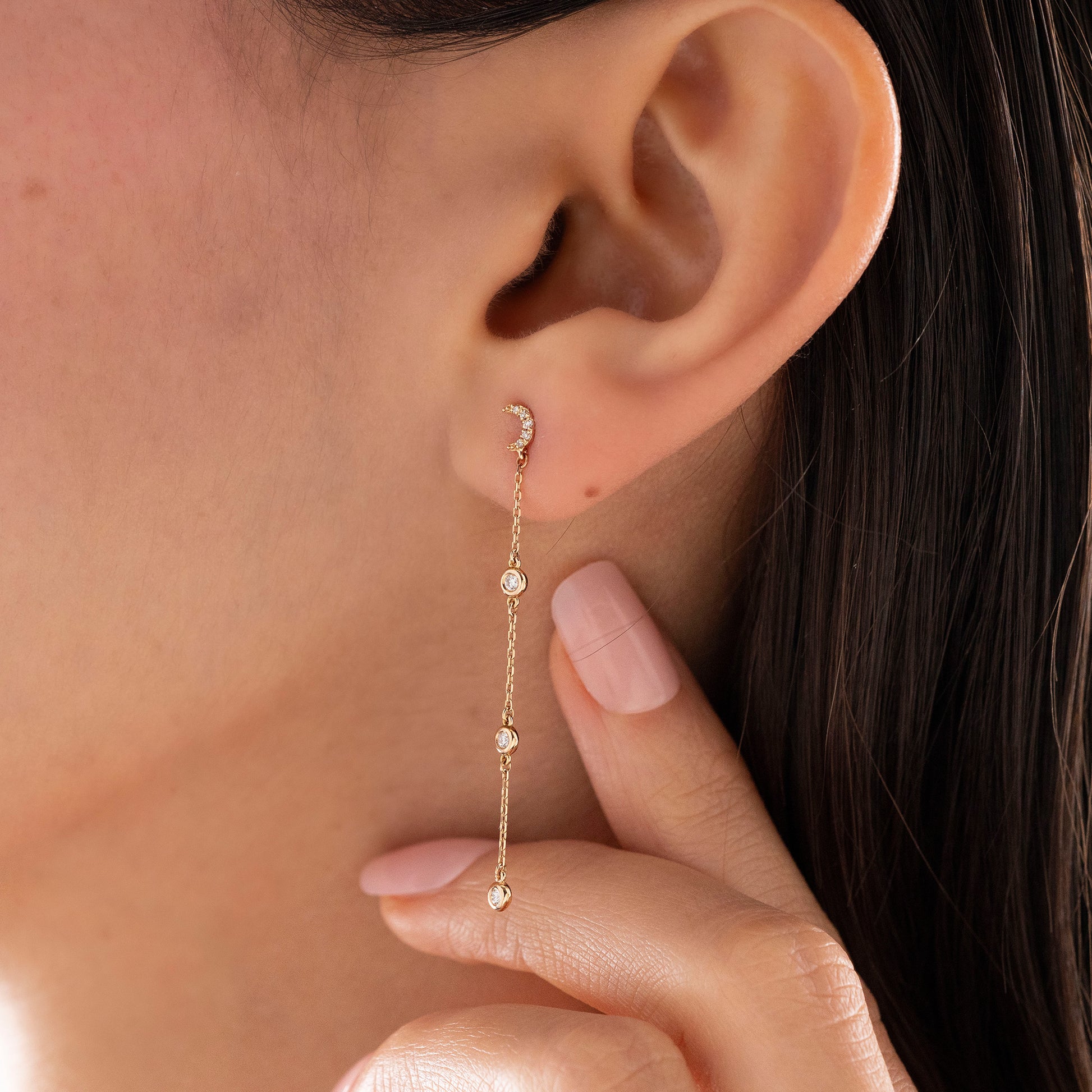 Arel Custom Jewelry 14k solid gold celestial crescent moon drop earring with dangling bezel set diamonds on a model.