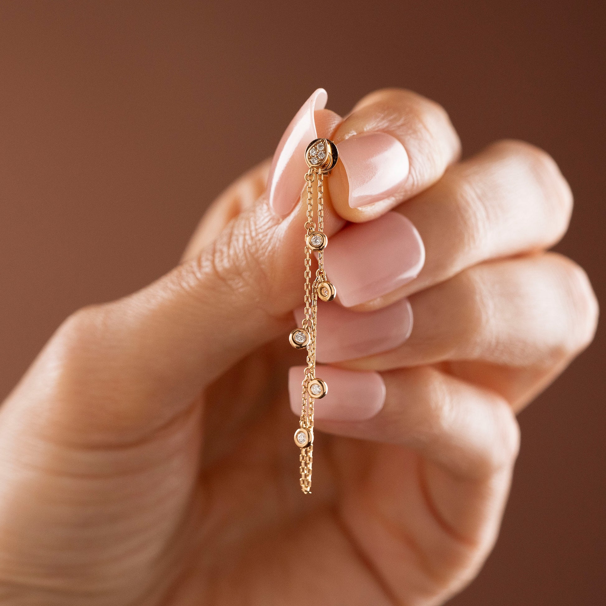 Arel Custom Jewelry 14k solid gold drape chain earring featuring a diamond teardrop stud and bezel diamonds on a model.