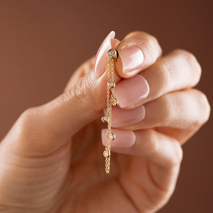 Arel Custom Jewelry 14k solid gold drape chain earring featuring a diamond teardrop stud and bezel diamonds on a model.