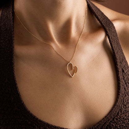 Arel Custom Jewelry 14k solid gold asymmetrical open heart necklace featuring half pave diamonds on a model.
