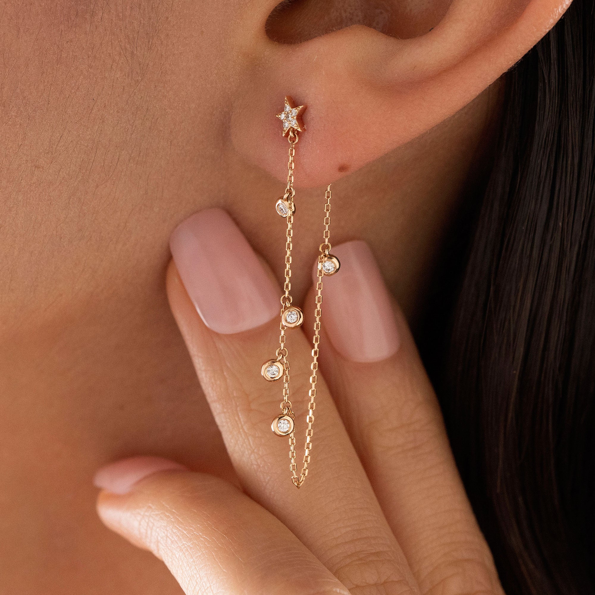 Dainty 14k gold front-to-back chain earring featuring a diamond star stud and bezel-set diamond drops on a model.