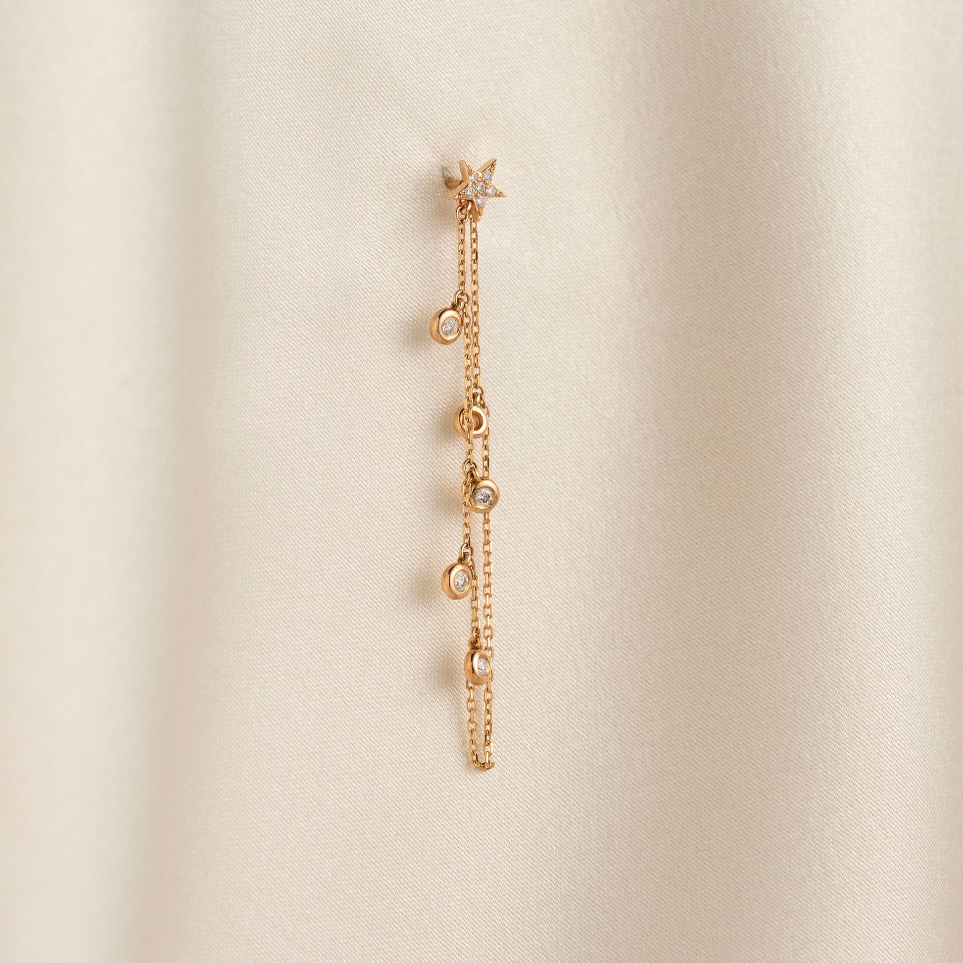 Dainty 14k gold front-to-back chain earring featuring a diamond star stud and bezel-set diamond drops on a model.