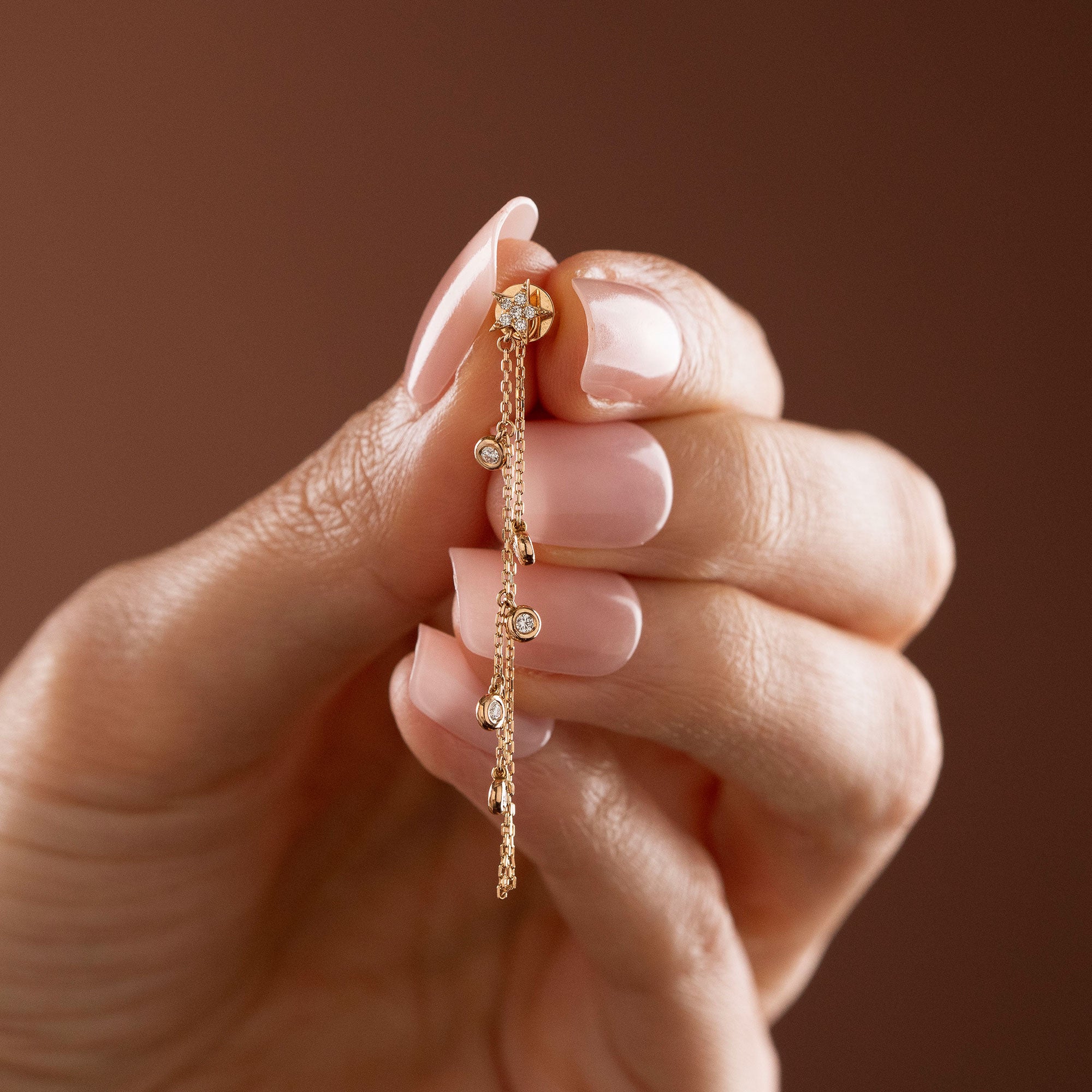 Dainty 14k gold front-to-back chain earring featuring a diamond star stud and bezel-set diamond drops on a model.
