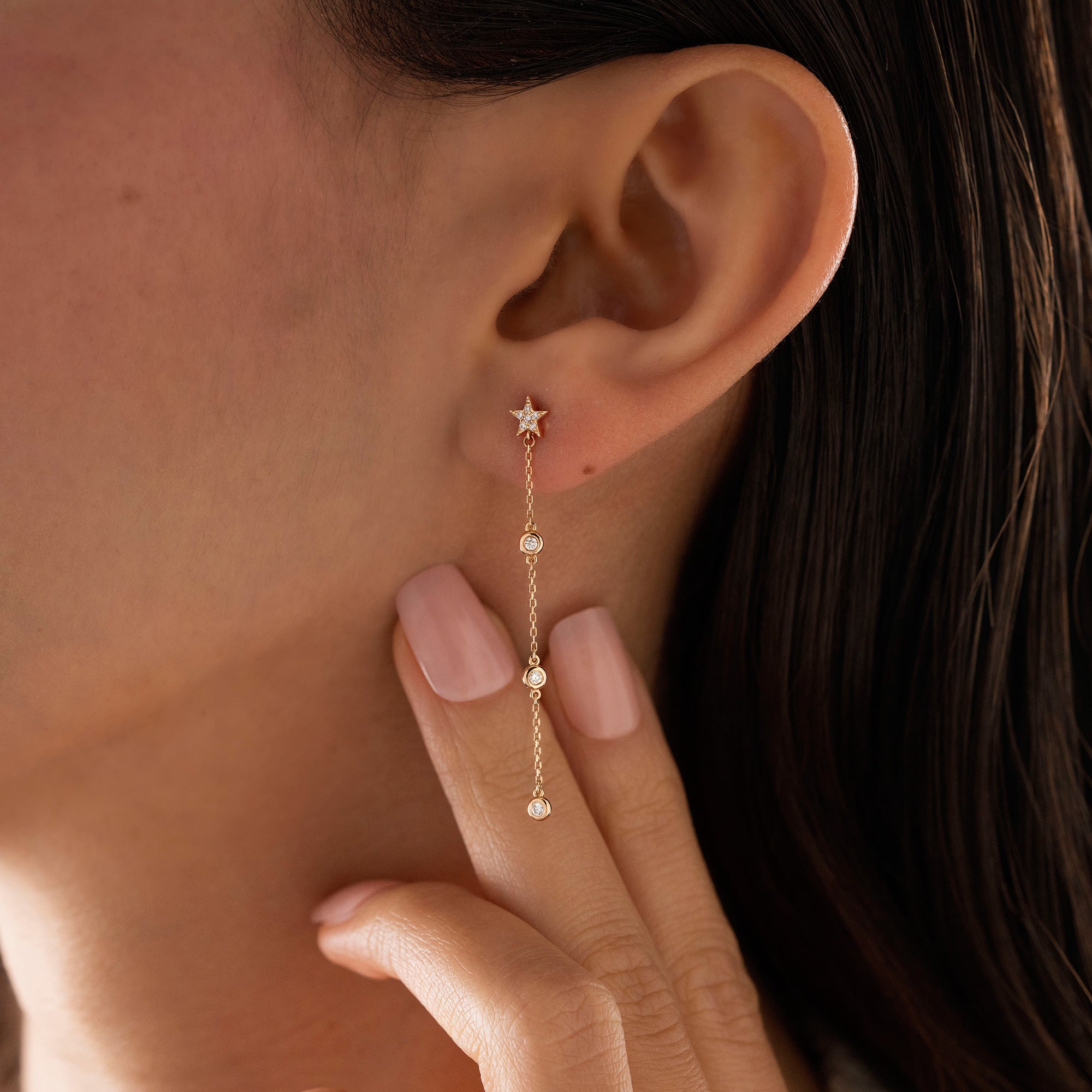 Arel Custom Jewelry 14k solid gold diamond star drop earring with dangling bezel set diamonds on a model.