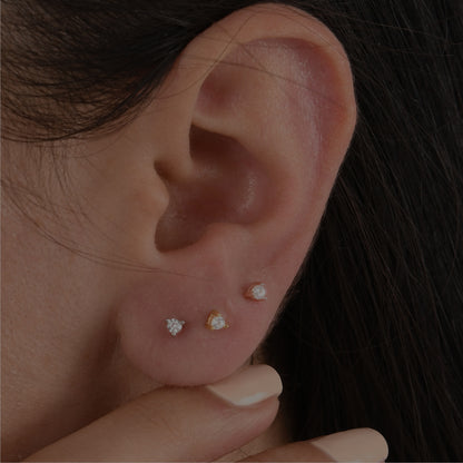 14k solid gold 3 prong diamond stud earrings featuring 2.20mm stones in rose, yellow, and white gold on a model's ear.