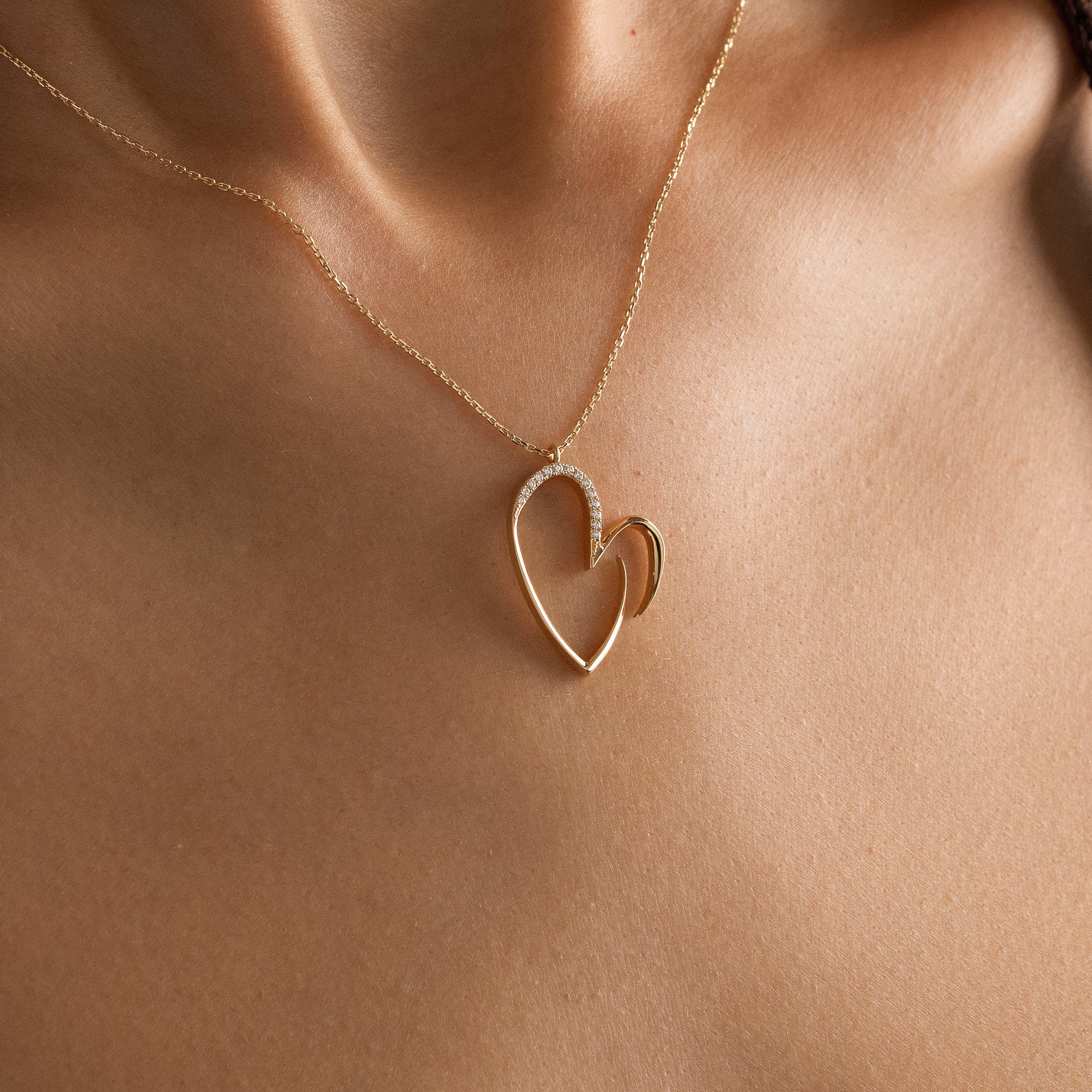 Arel Custom Jewelry 14k solid gold asymmetrical open heart necklace featuring half pave diamonds on a model.