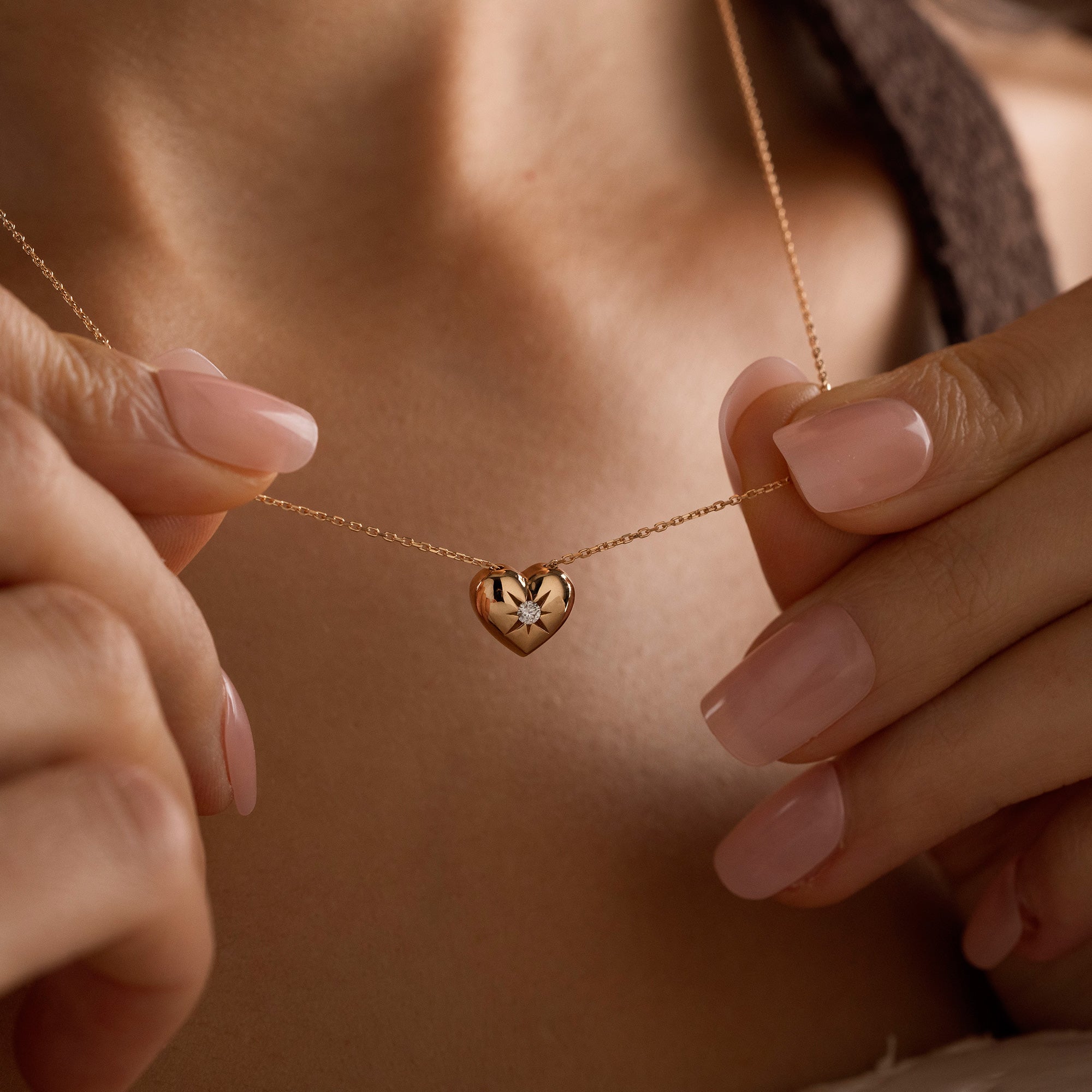 Arel Custom Jewelry 14k solid gold necklace featuring a polished puffed heart pendant with a starburst set center diamond on a model.