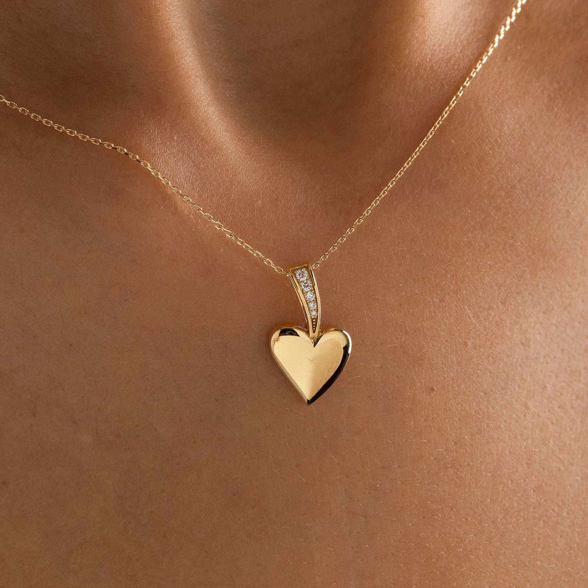 Arel Custom Jewelry 14k solid gold polished heart pendant featuring a pave diamond bail on a model.