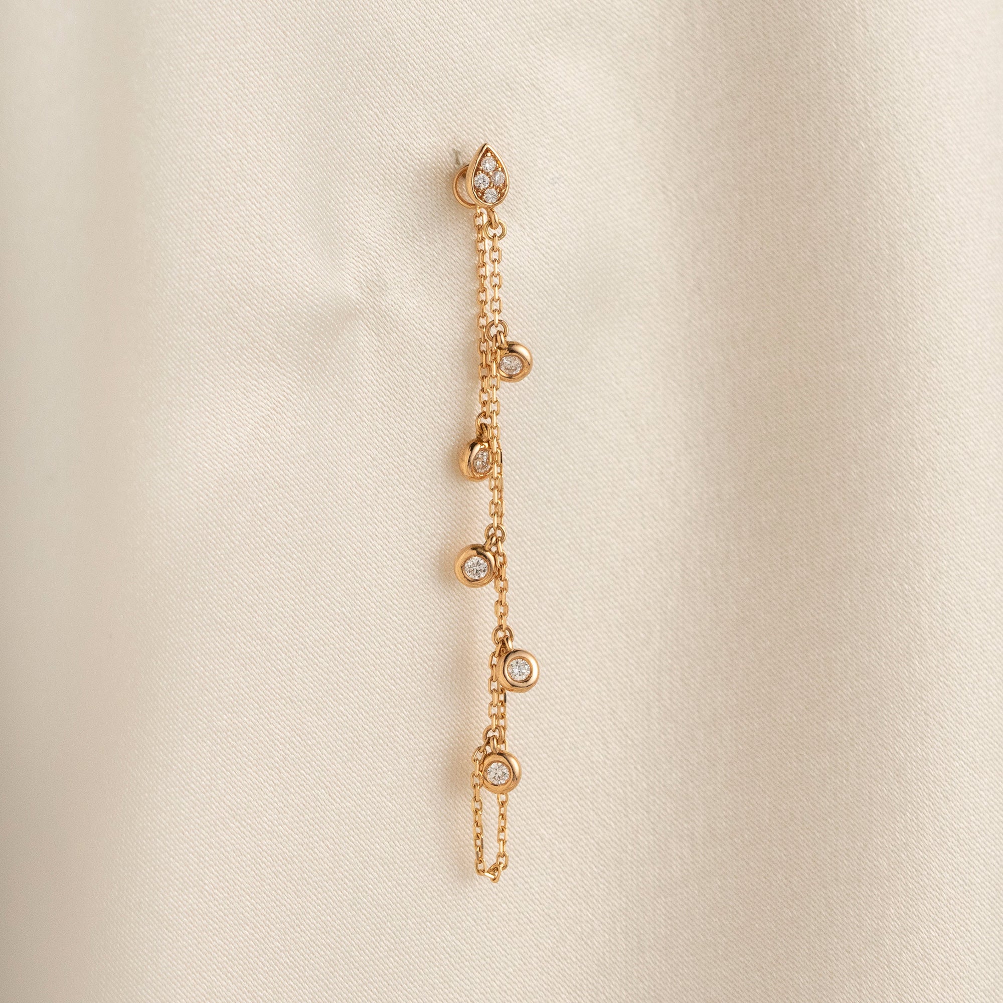 Arel Custom Jewelry 14k solid gold drape chain earring featuring a diamond teardrop stud and bezel diamonds on a model.