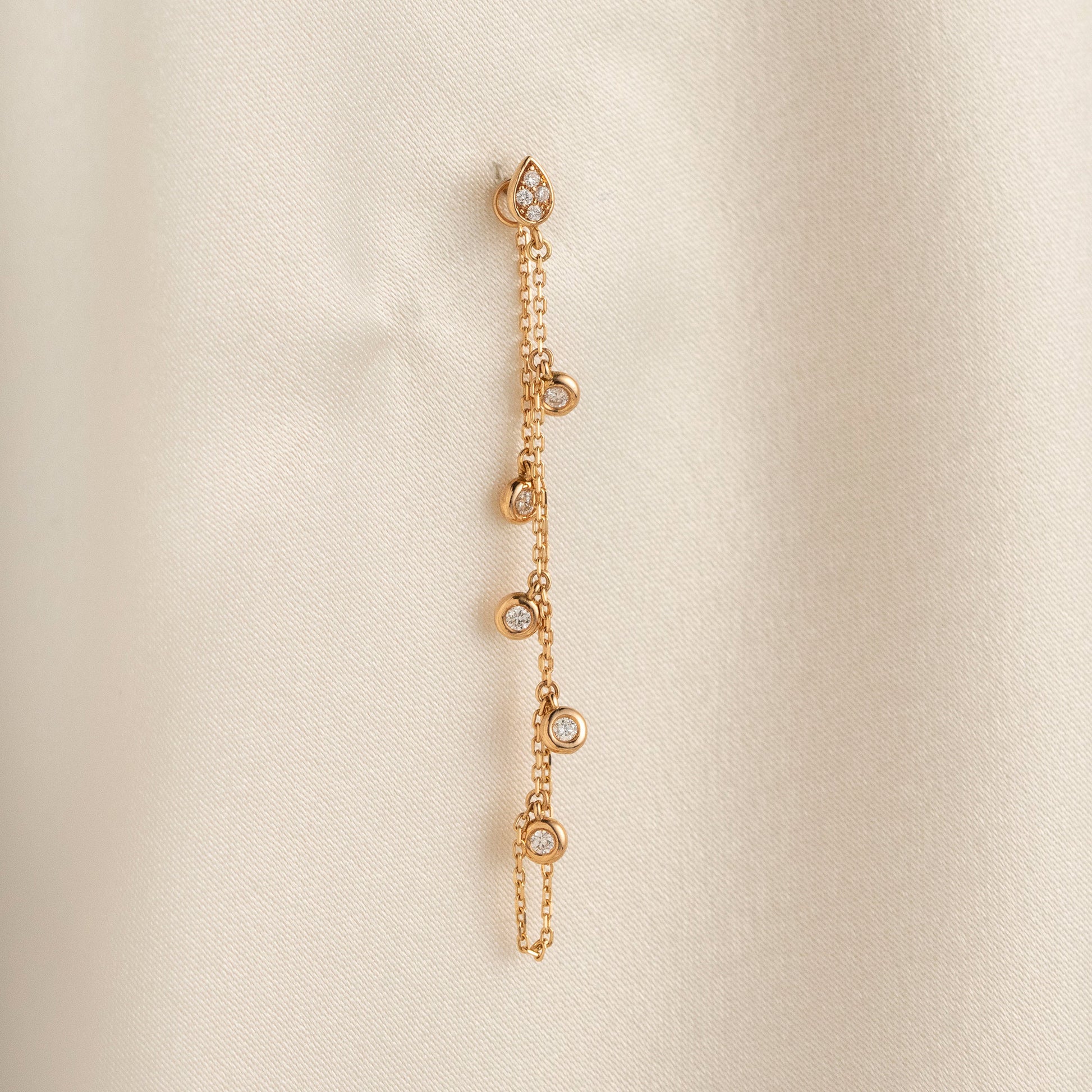 Arel Custom Jewelry 14k solid gold drape chain earring featuring a diamond teardrop stud and bezel diamonds on a model.