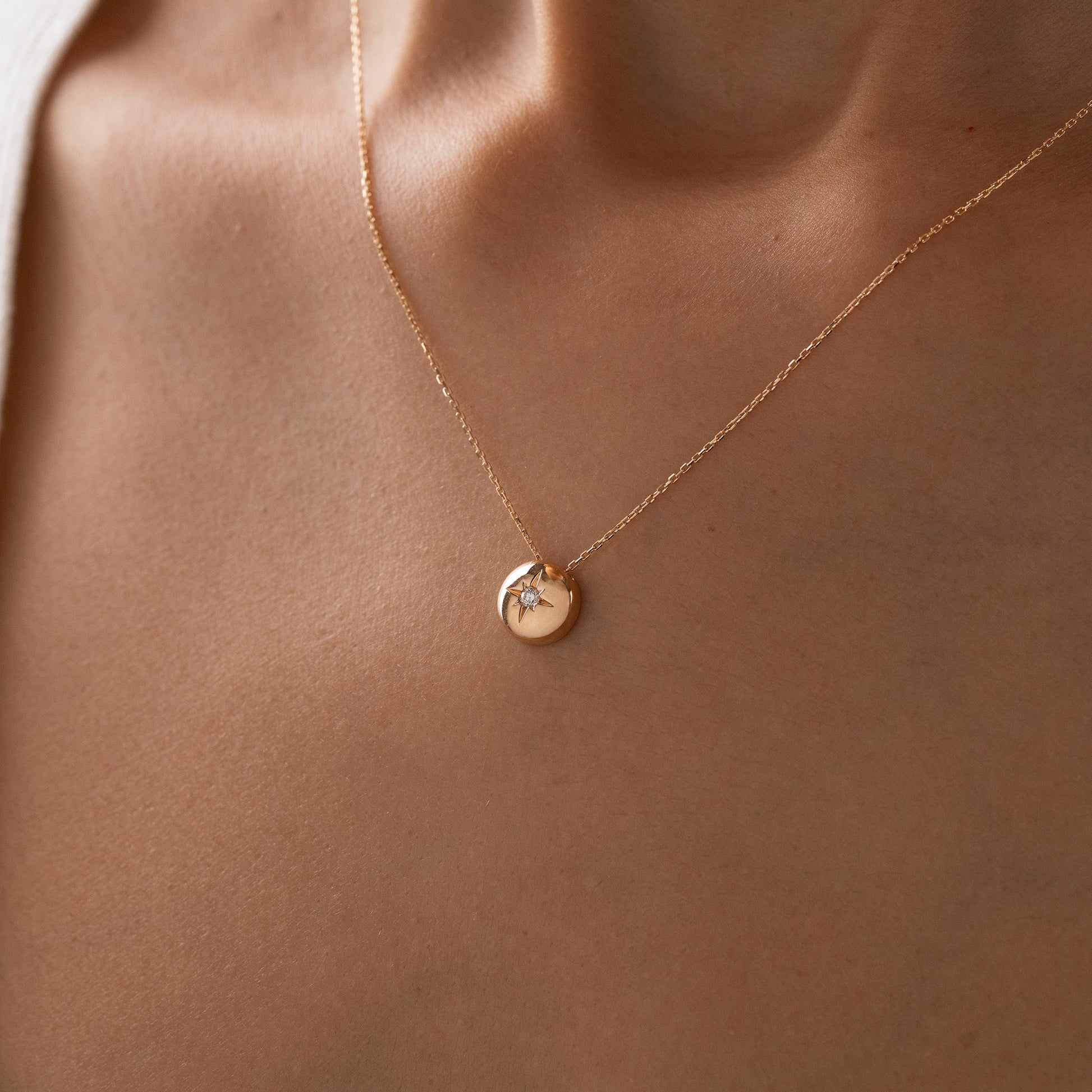 Arel Custom Jewelry 14k solid gold necklace featuring a polished domed pendant with a starburst set center diamond on a model.