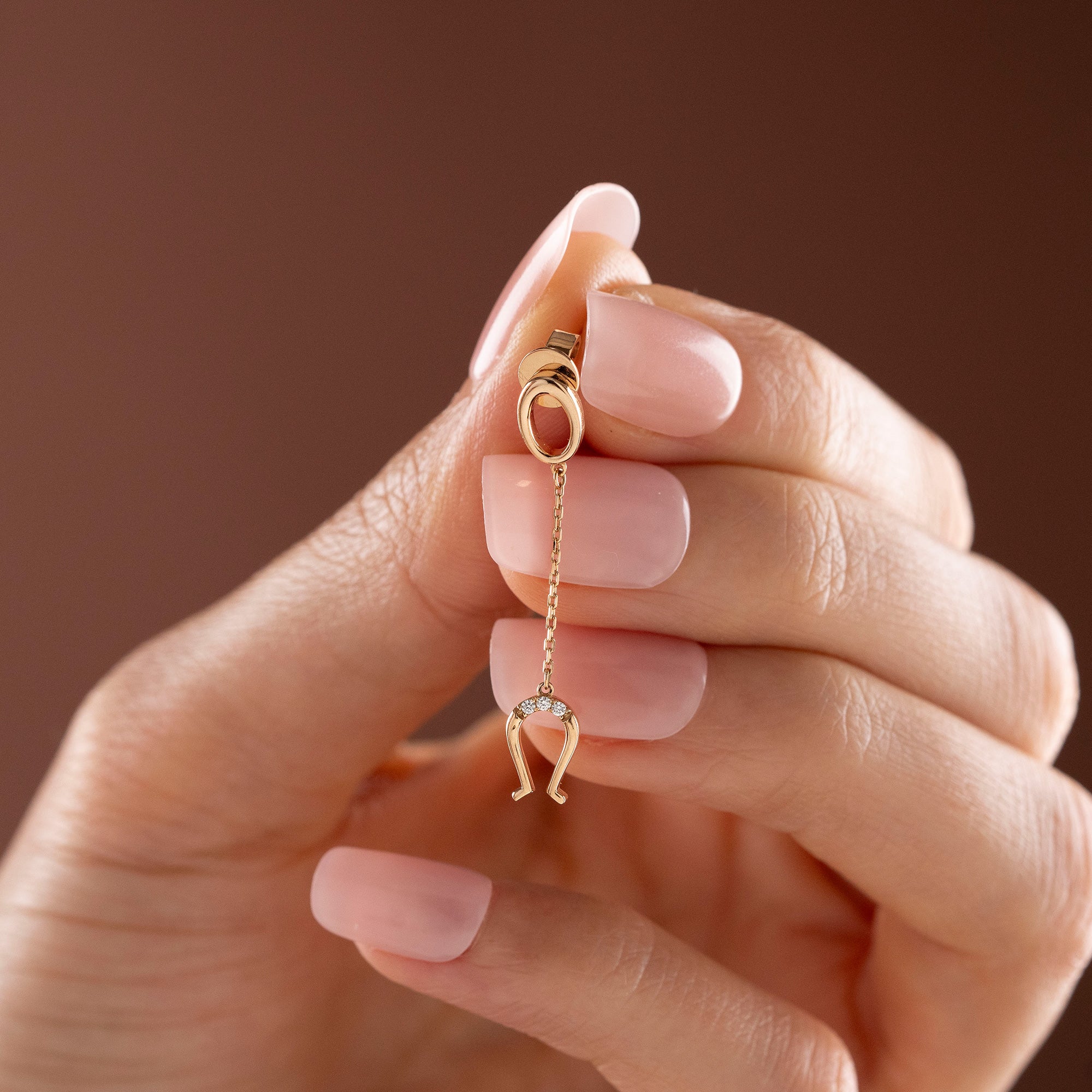 Arel Custom Jewelry 14k solid gold drop earring featuring an oval loop stud and dangling diamond horseshoe charm on a model.