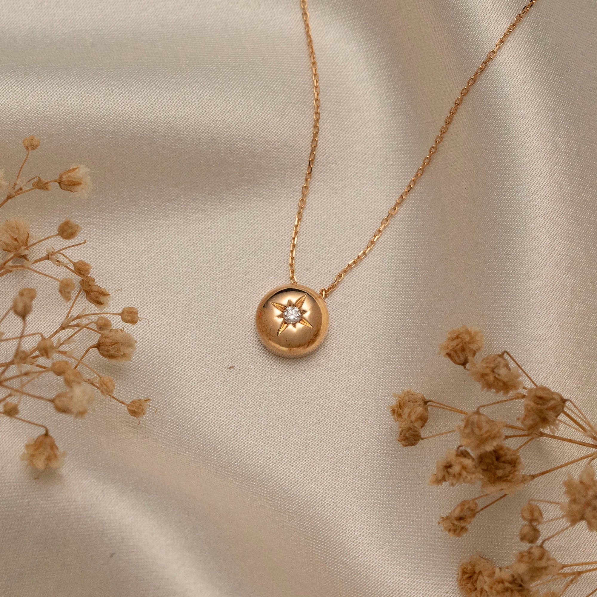 Arel Custom Jewelry 14k solid gold necklace featuring a polished domed pendant with a starburst set center diamond on a model.