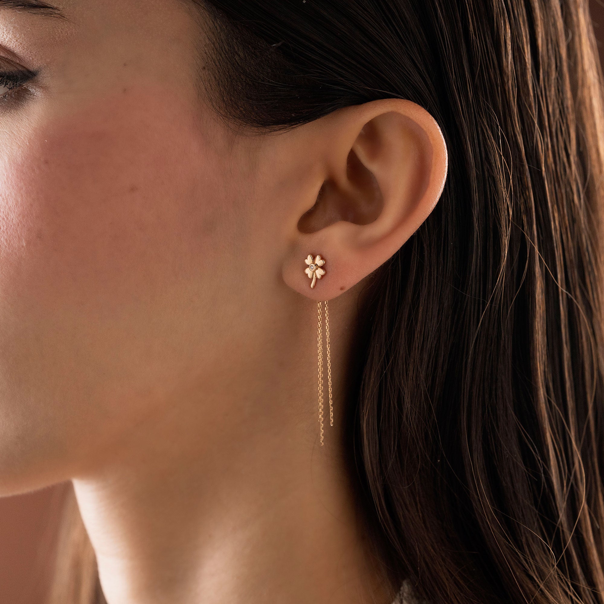Arel Custom Jewelry 14k solid gold clover earrings with a center diamond and dangling chains on model's ear.