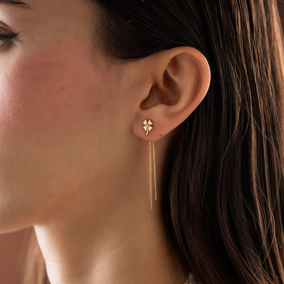 Arel Custom Jewelry 14k solid gold clover earrings with a center diamond and dangling chains on model's ear.