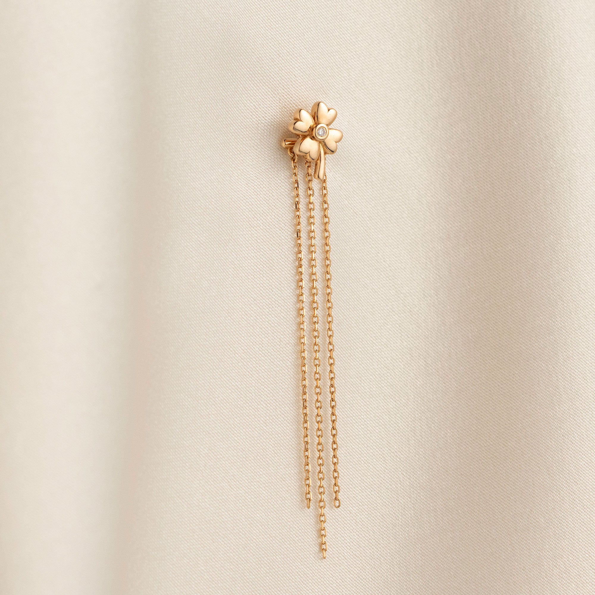 Arel Custom Jewelry 14k solid gold clover earrings with a center diamond and dangling chains on model's ear.