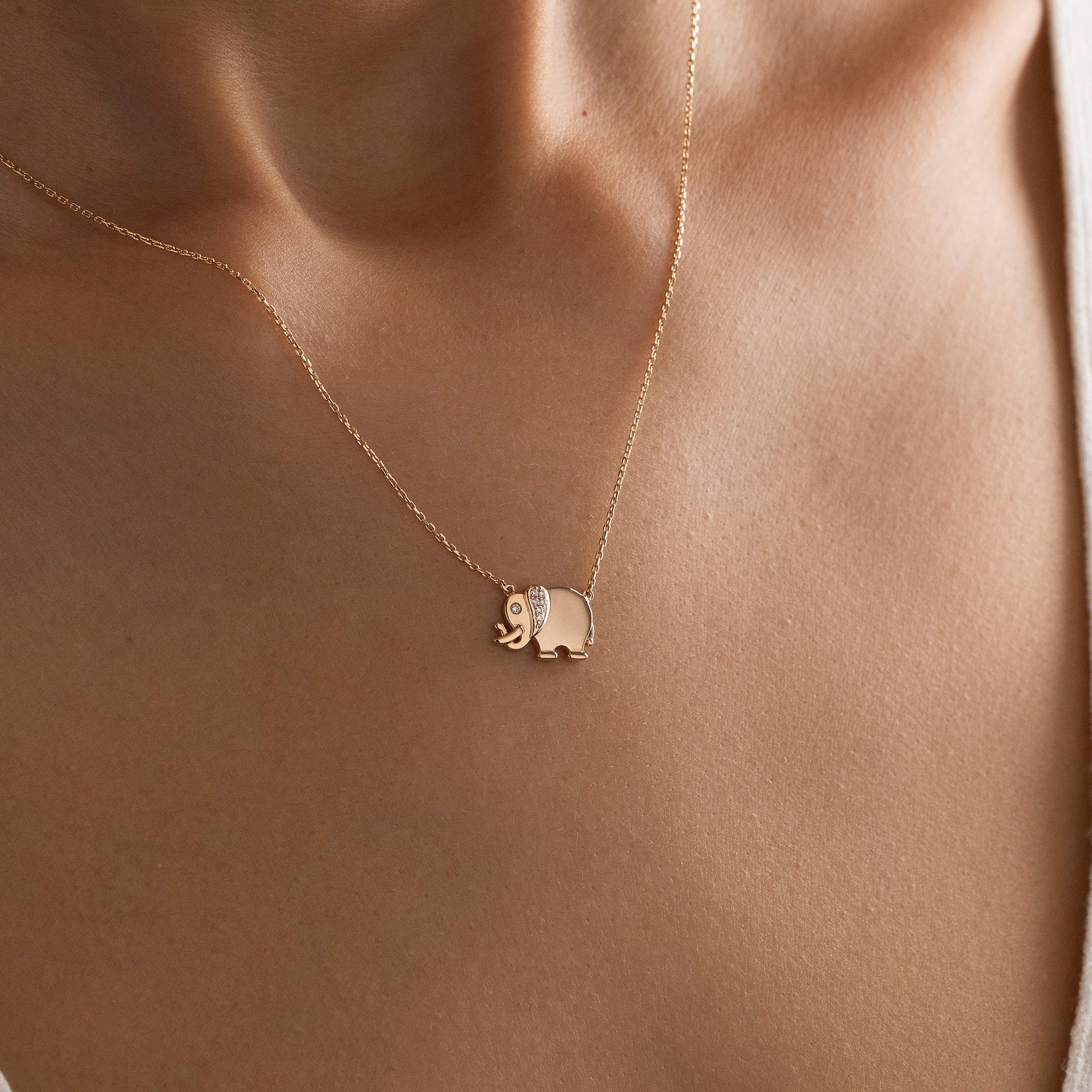 Arel Custom Jewelry 14k solid gold necklace featuring a polished elephant pendant with a pave diamond ear and trunk up on a model.