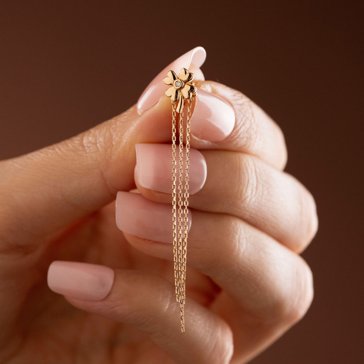 Arel Custom Jewelry 14k solid gold clover earrings with a center diamond and dangling chains on model's ear.