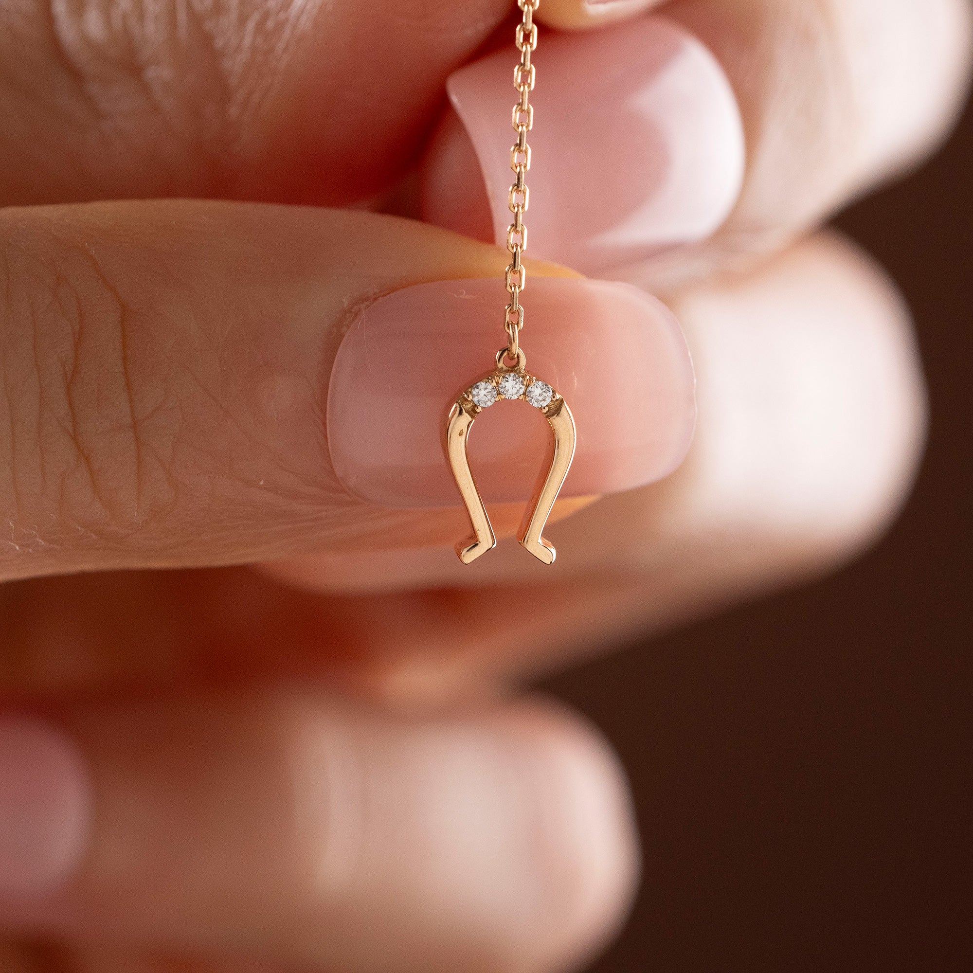 Arel Custom Jewelry 14k solid gold drop earring featuring an oval loop stud and dangling diamond horseshoe charm on a model.