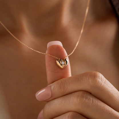 Arel Custom Jewelry 14k solid gold necklace featuring a polished puffed heart pendant with a starburst set center diamond on a model.