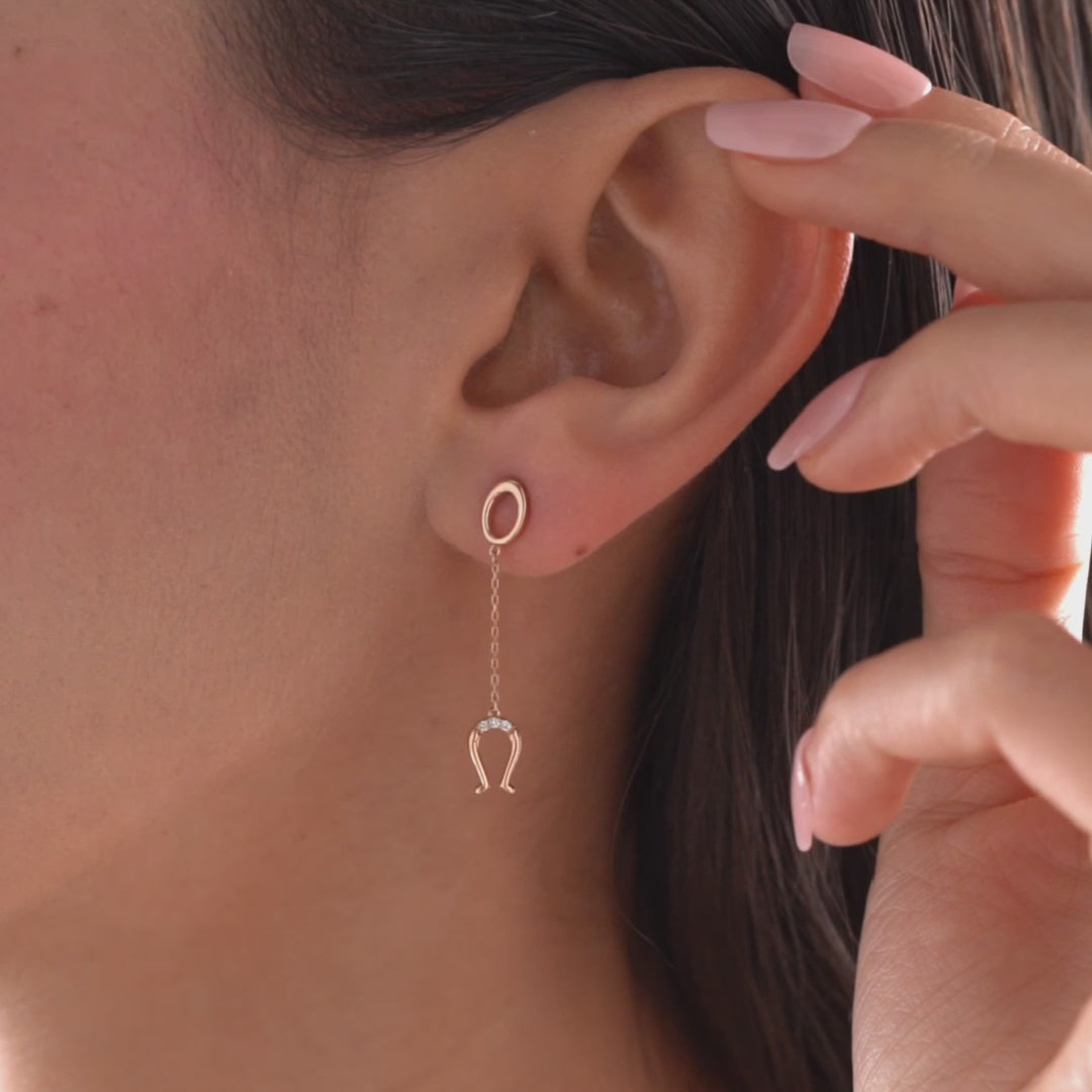 Arel Custom Jewelry 14k solid gold drop earring featuring an oval loop stud and dangling diamond horseshoe charm on a model.