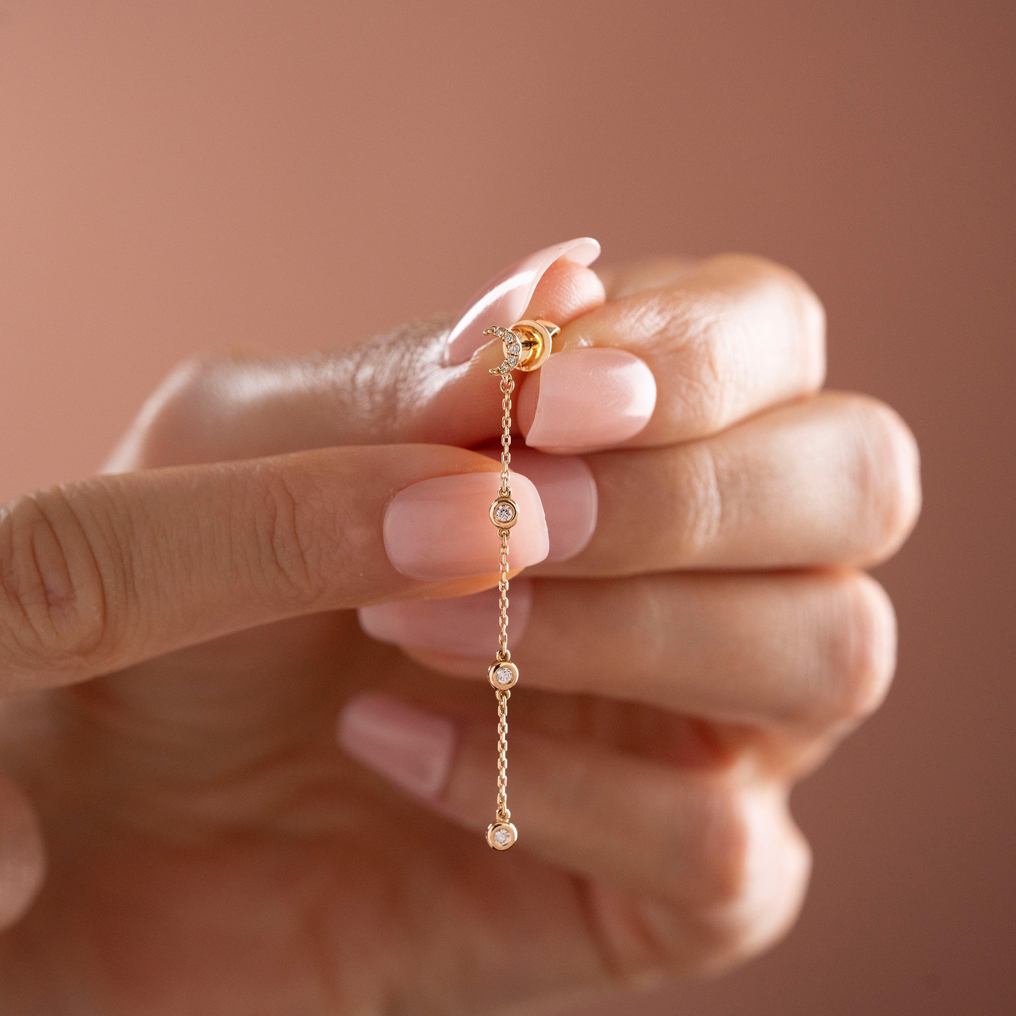 Arel Custom Jewelry 14k solid gold celestial crescent moon drop earring with dangling bezel set diamonds on a model.