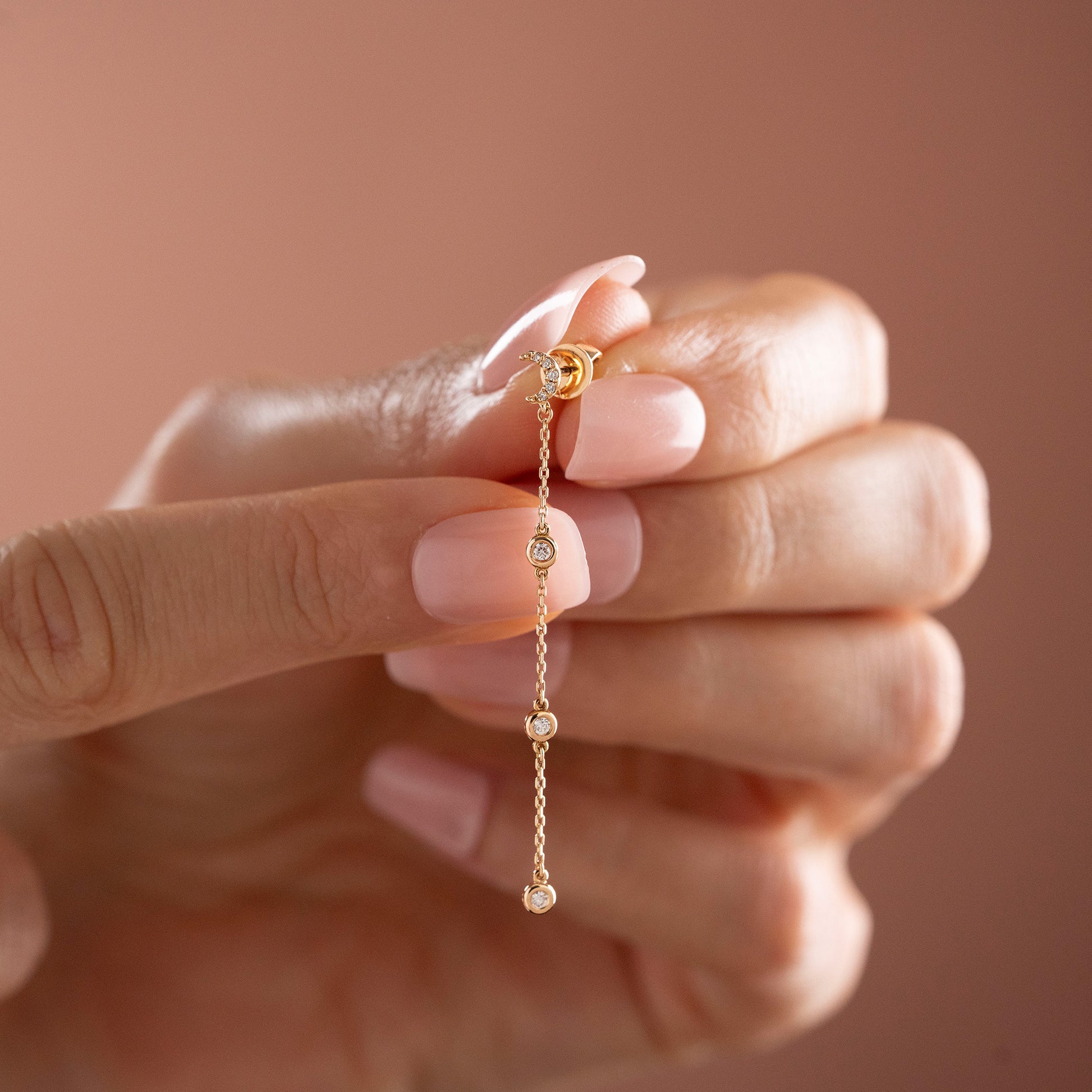 Arel Custom Jewelry 14k solid gold celestial crescent moon drop earring with dangling bezel set diamonds on a model.