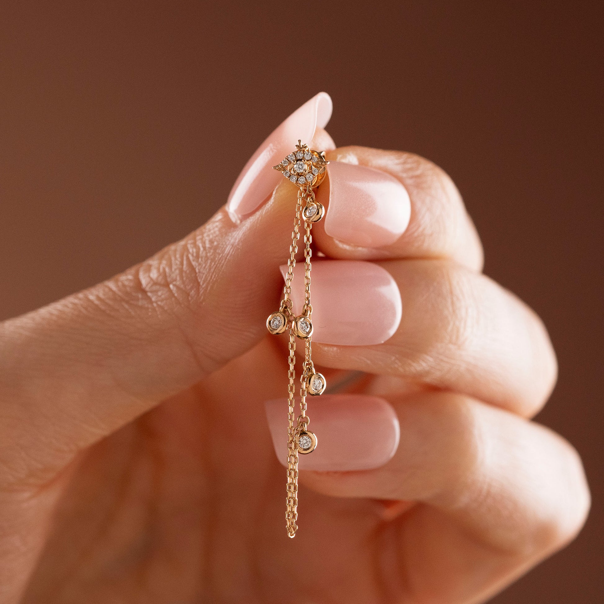 Arel Custom Jewelry 14k solid gold drape chain earring featuring a pave diamond evil eye stud and bezel diamonds on a model.
